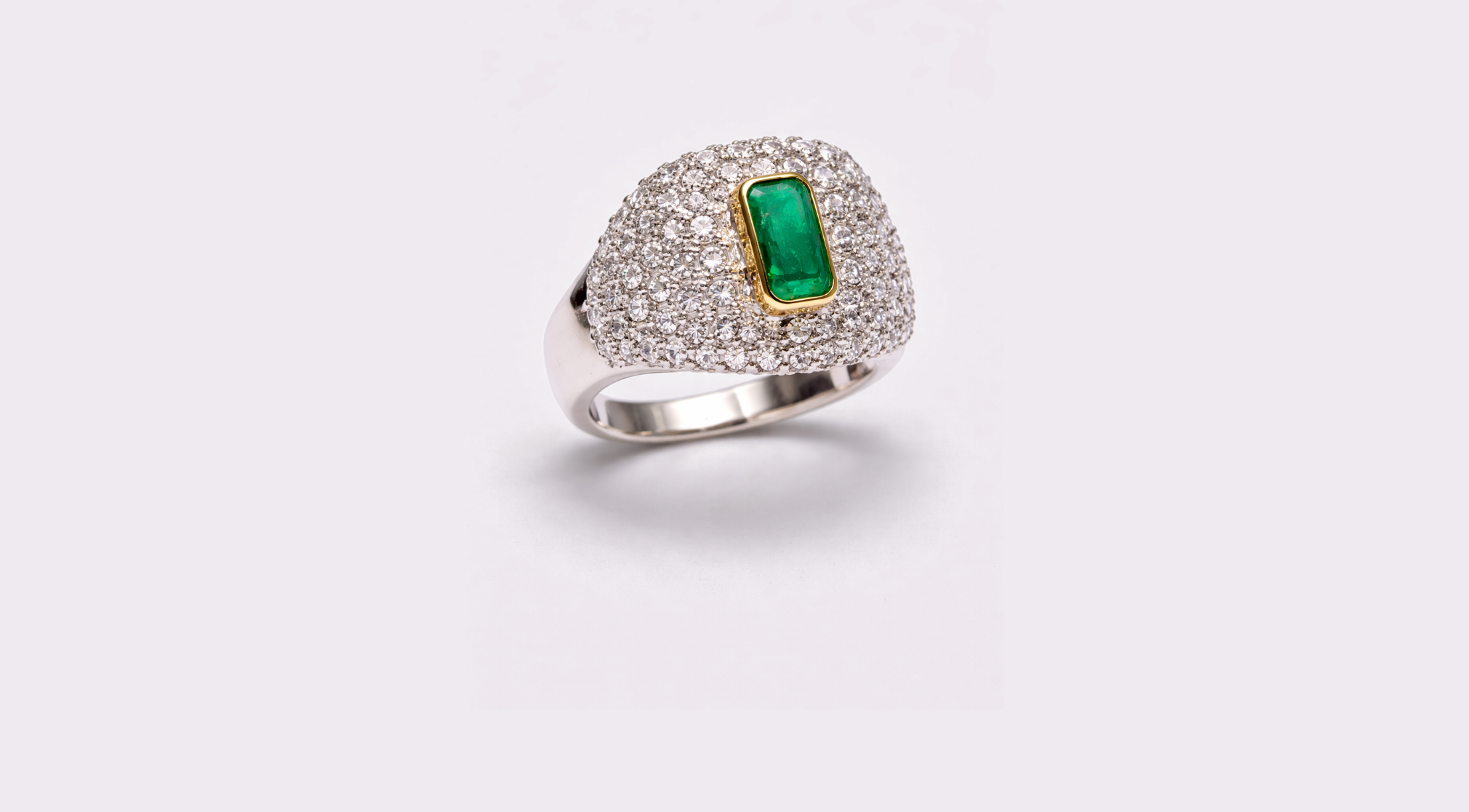 A silver ring featuring a large rectangular green gemstone set in a gold bezel, surrounded by numerous small diamonds on the band