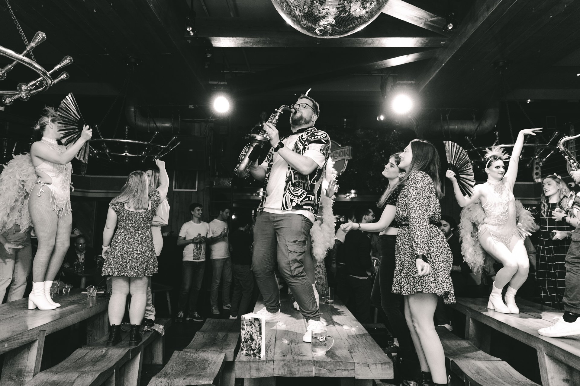 People dancing and playing saxophones in a lively club called Brewhemia in Edinburgh, surrounded by performers with fans.