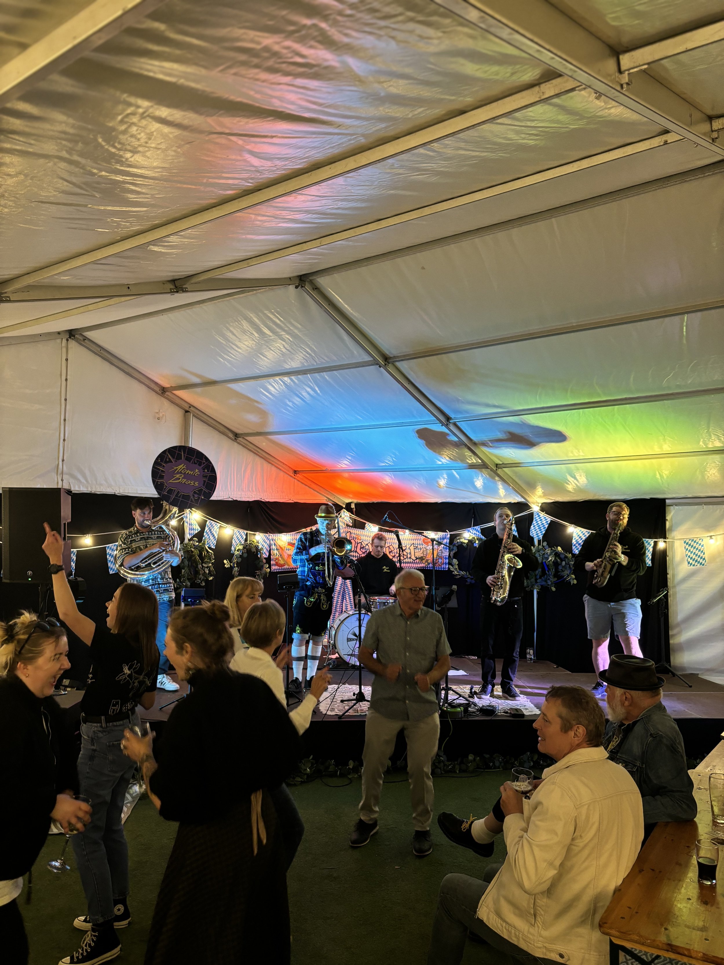 People dancing and enjoying live band performance at a beer festival in a tent with colorful lighting.