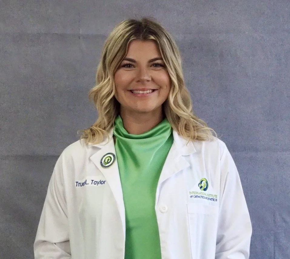 Person in a white lab coat with logos, smiling against a gray background.