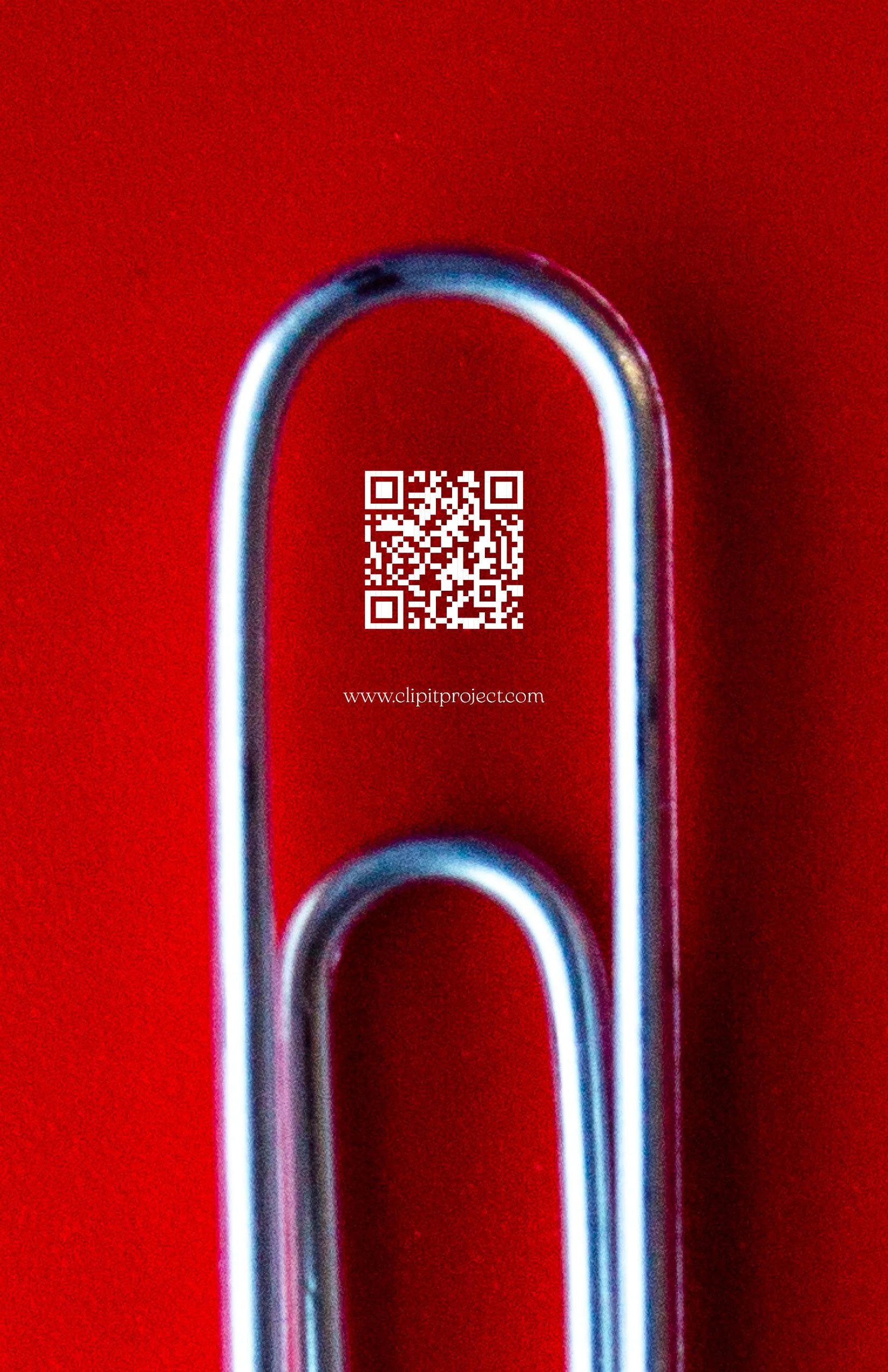 Close-up of metallic paperclip with a QR code sticker on a red background.