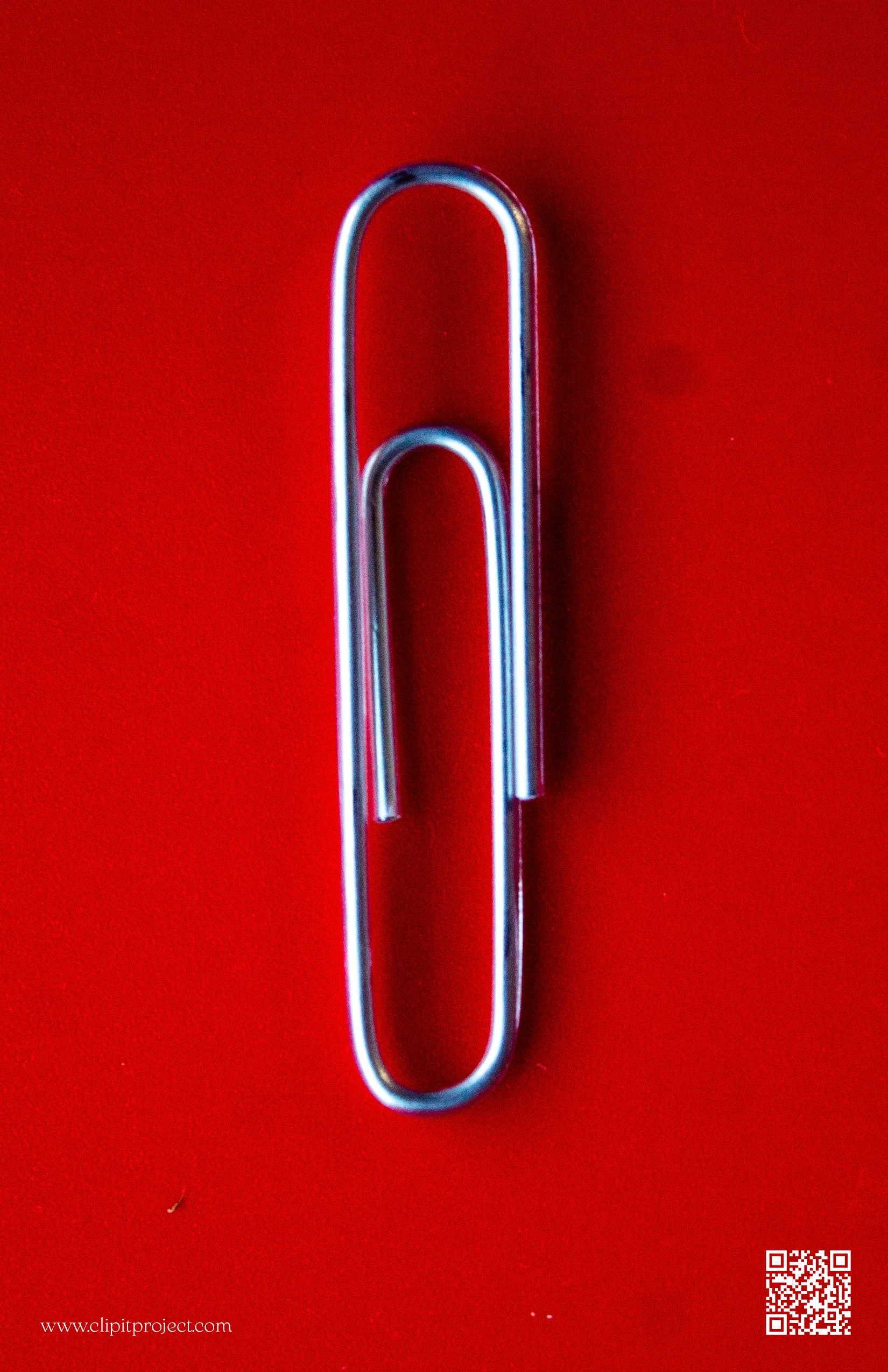 Close-up of a metallic paperclip on a red background with a QR code and website URL in the lower corners.