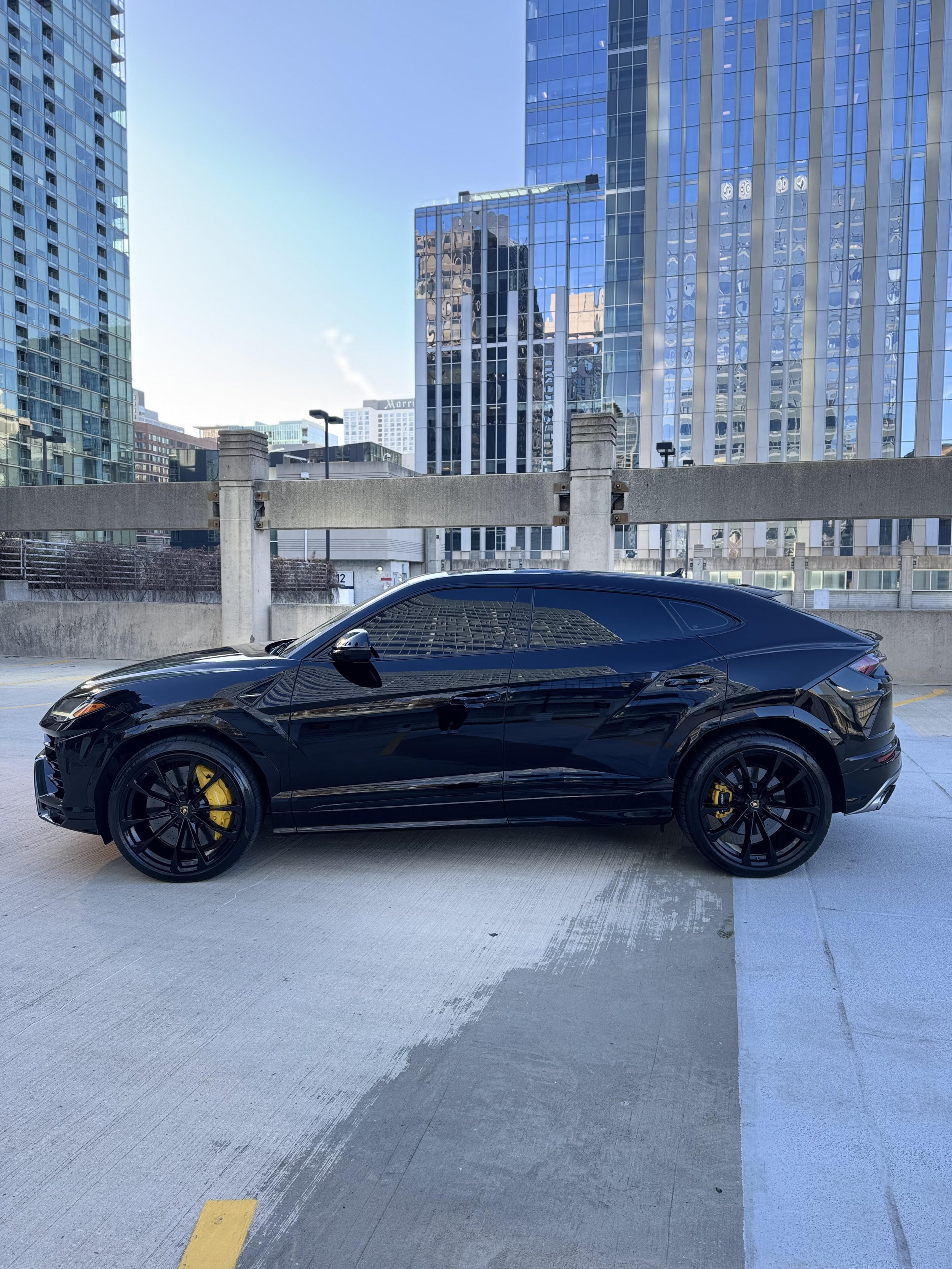 Black luxury SUV parked on rooftop with city skyscrapers in background.