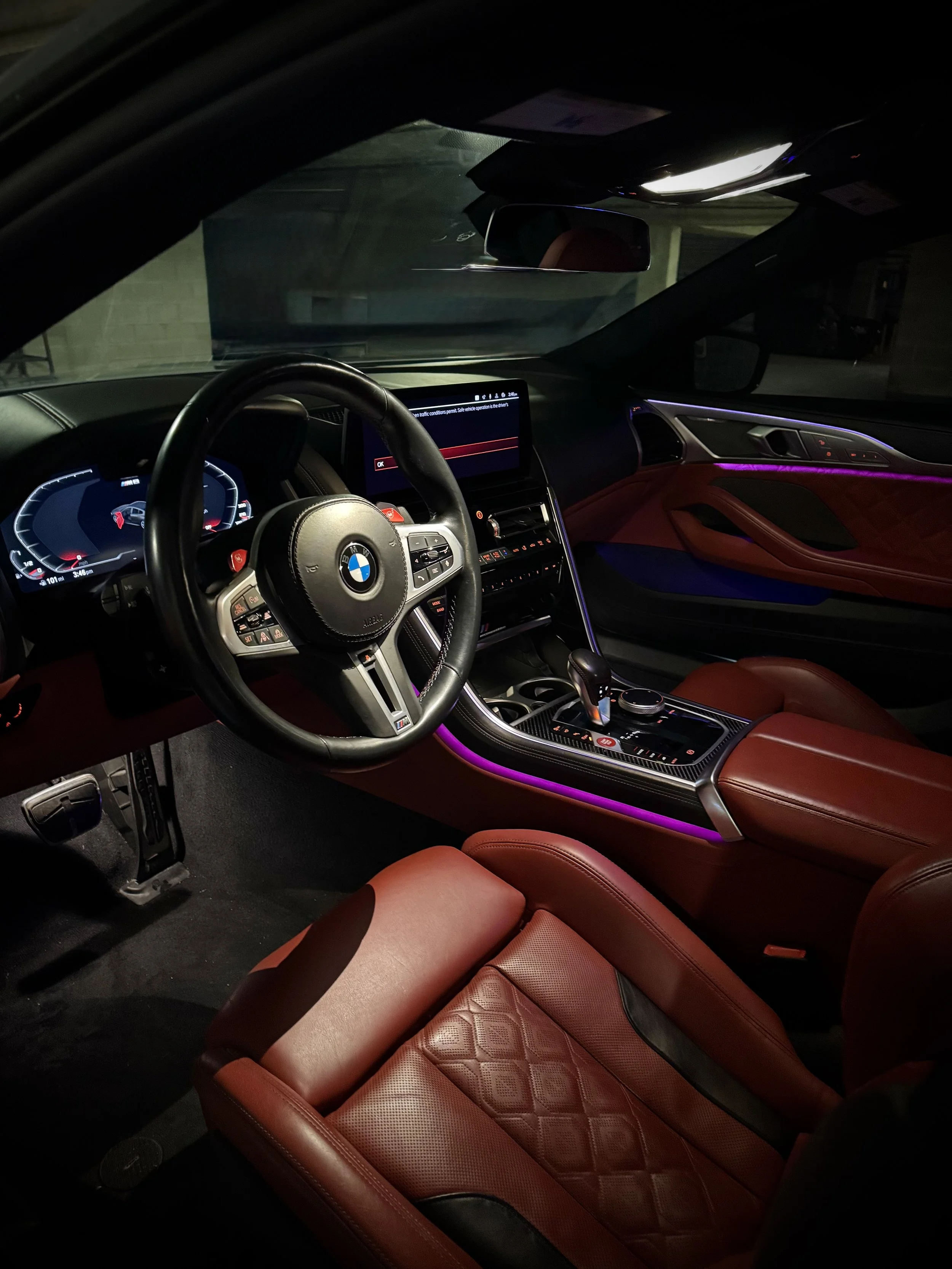 BMW M8 Competition in Nardo Gray with red leather interior and custom starlight ceiling parked outdoors.