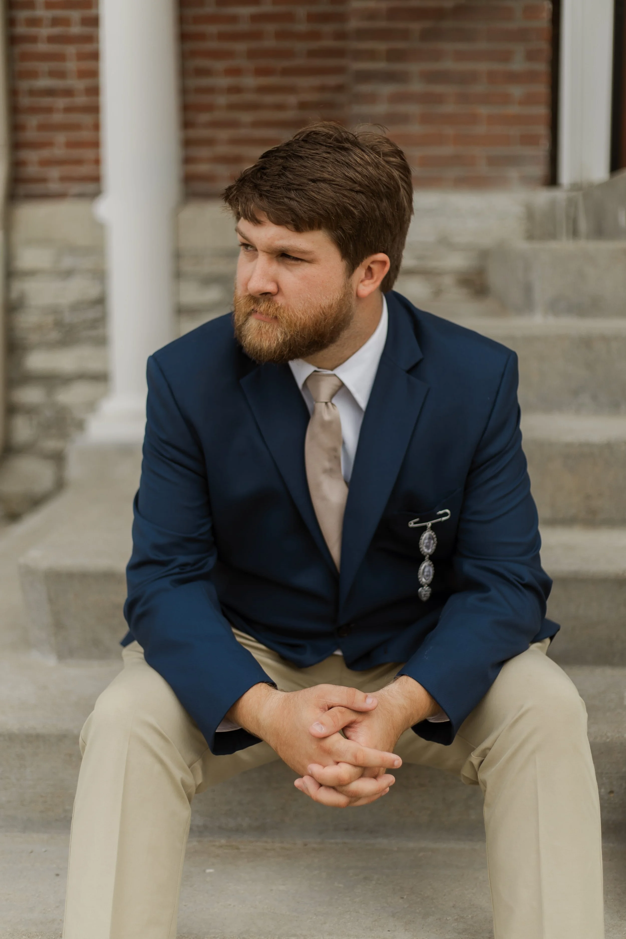 Wedding photography of a groom seated on stone steps outside a brick wedding venue, captured by a Florence, KY wedding photographer specializing in natural and timeless wedding portraits.