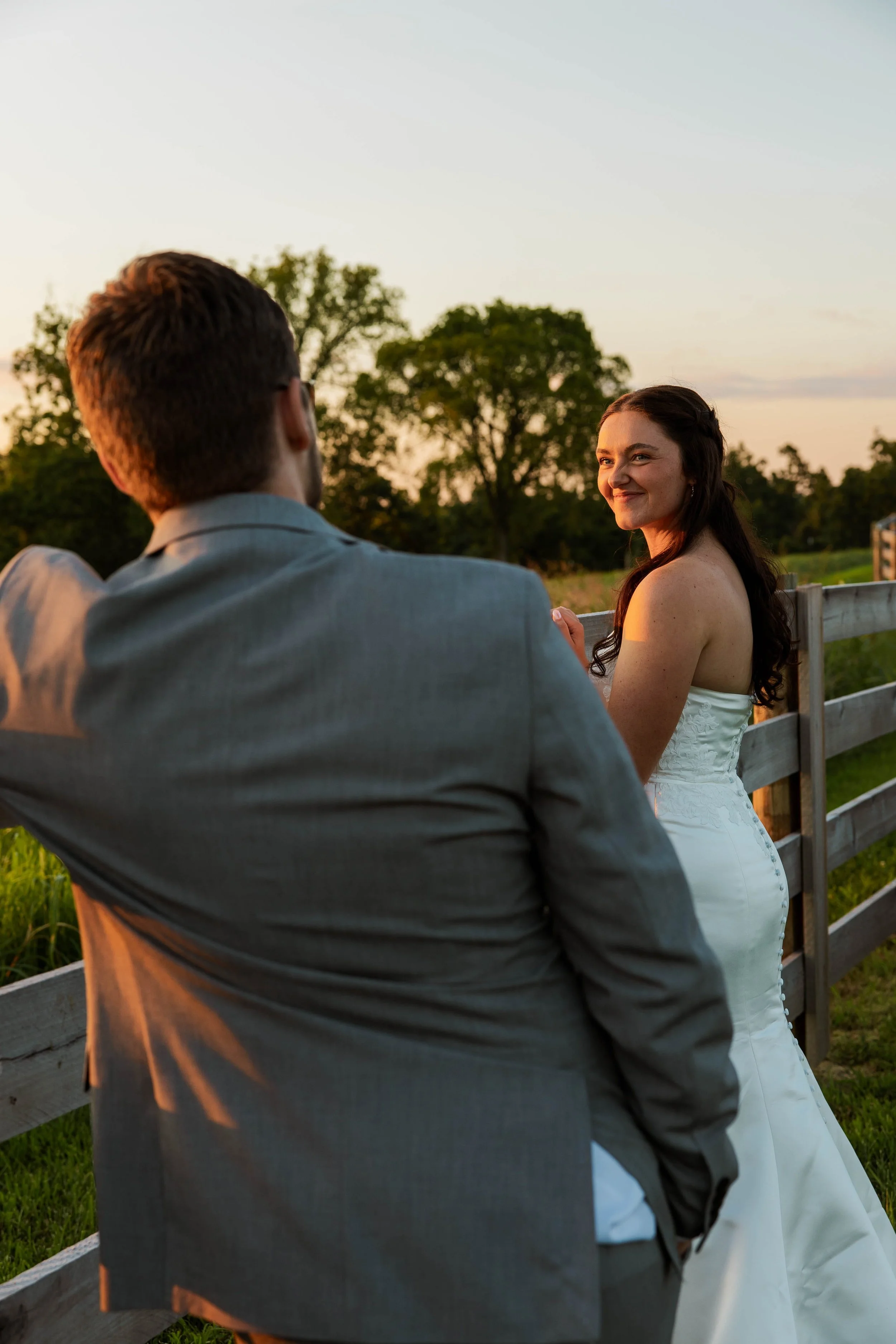 Outdoor wedding photography of a bride and groom sharing a quiet moment at golden hour near a wooden fence