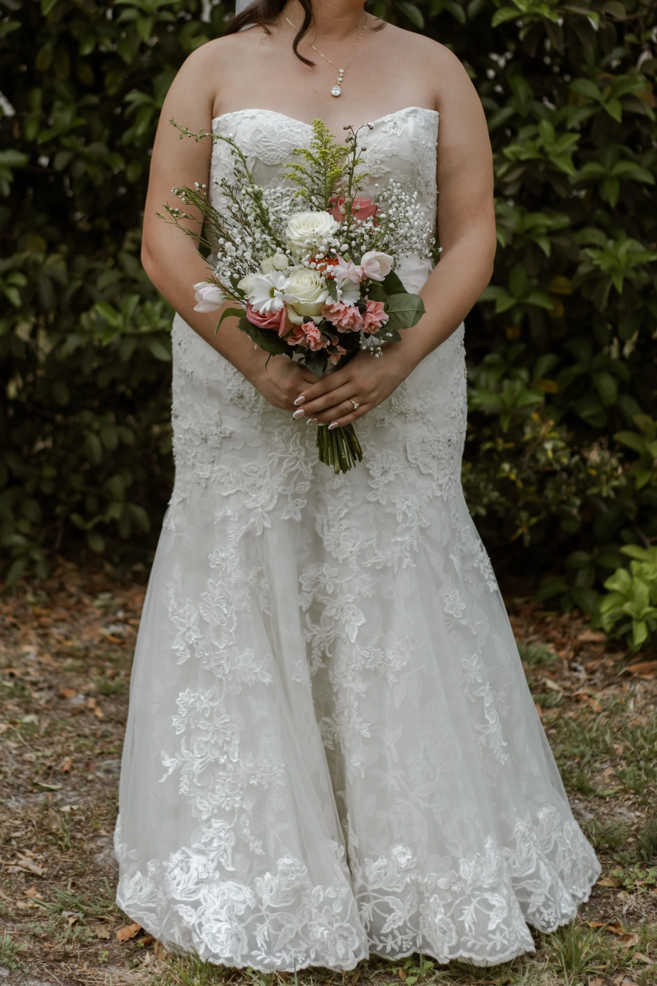 Wedding photography of a bride holding a floral bouquet while wearing a lace wedding dress, photographed outdoors during bridal portraits at a wedding venue.