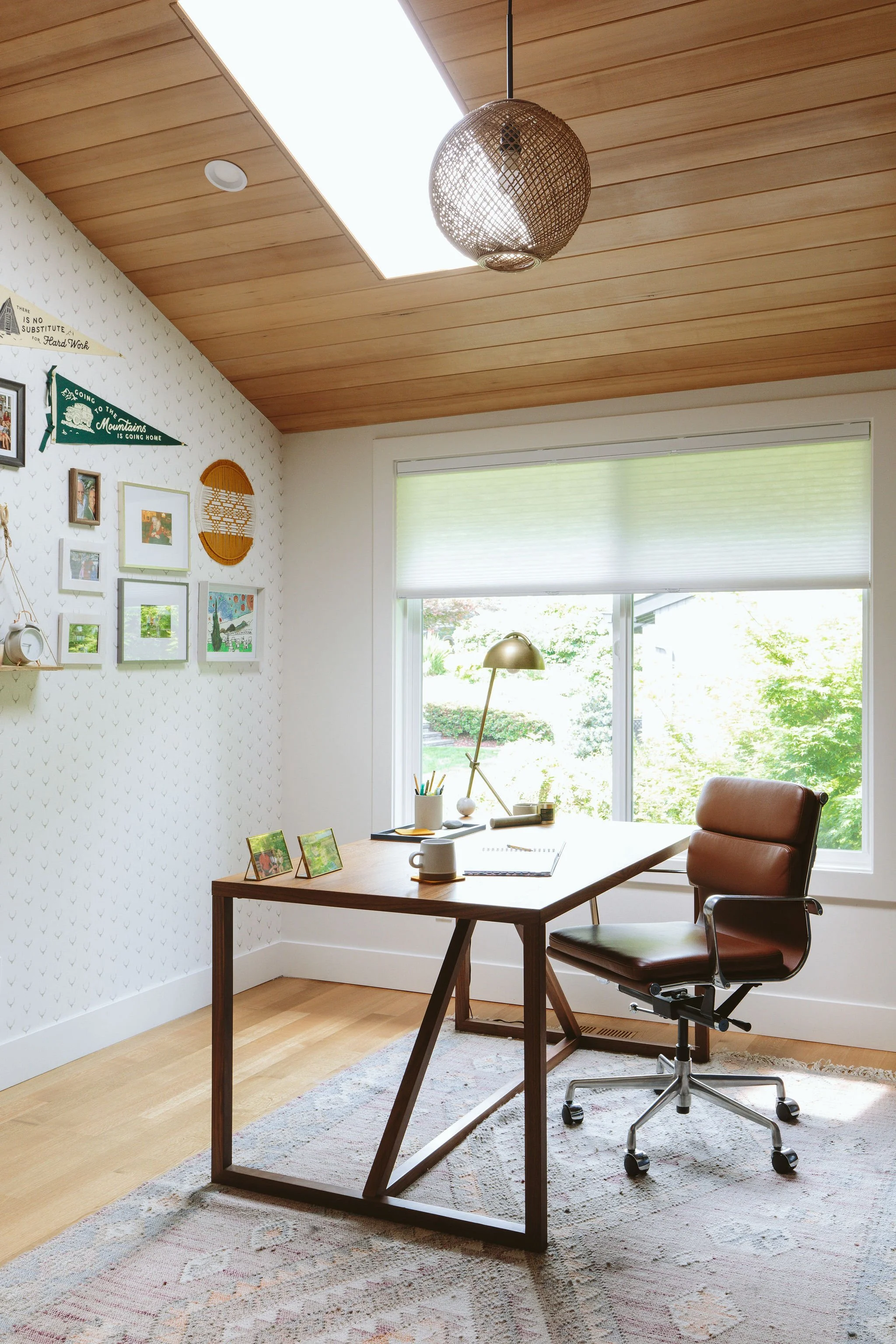 Home office furnished and decorated by Interior Designer Alana Spears. The office features a wood tongue and groover ceiling, office desk and chair and wallpaper with a mixed media art gallery.
