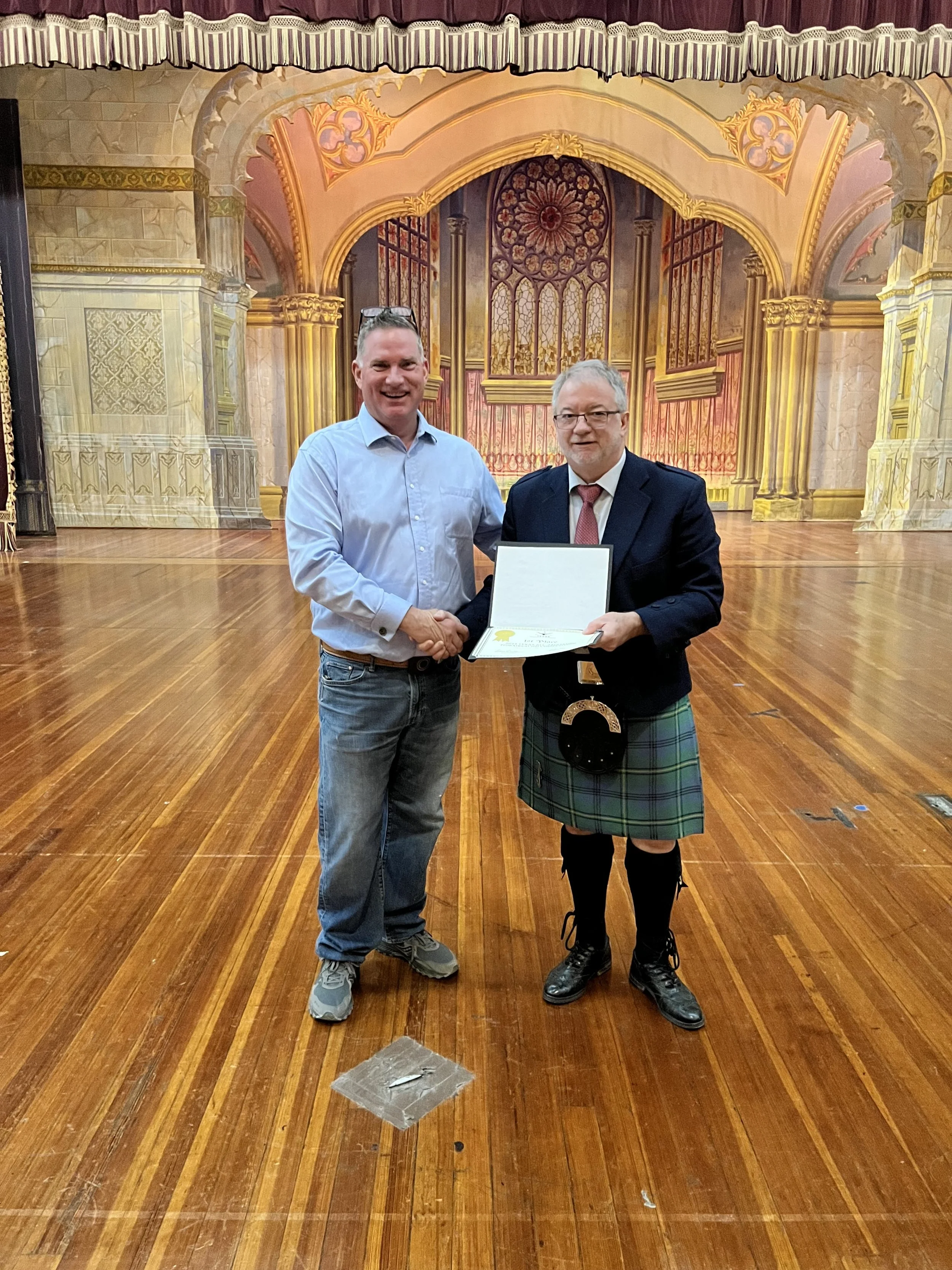 Two men shaking hands standing in front of a decorated stage with a wooden floor.