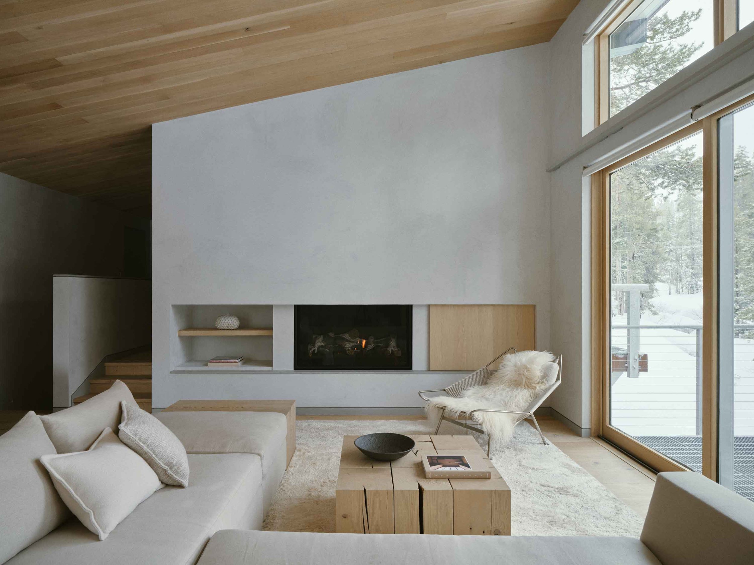 Luxury alpine living room with neutral tones, layered textures, sculptural furniture, and large windows overlooking a mountain landscape