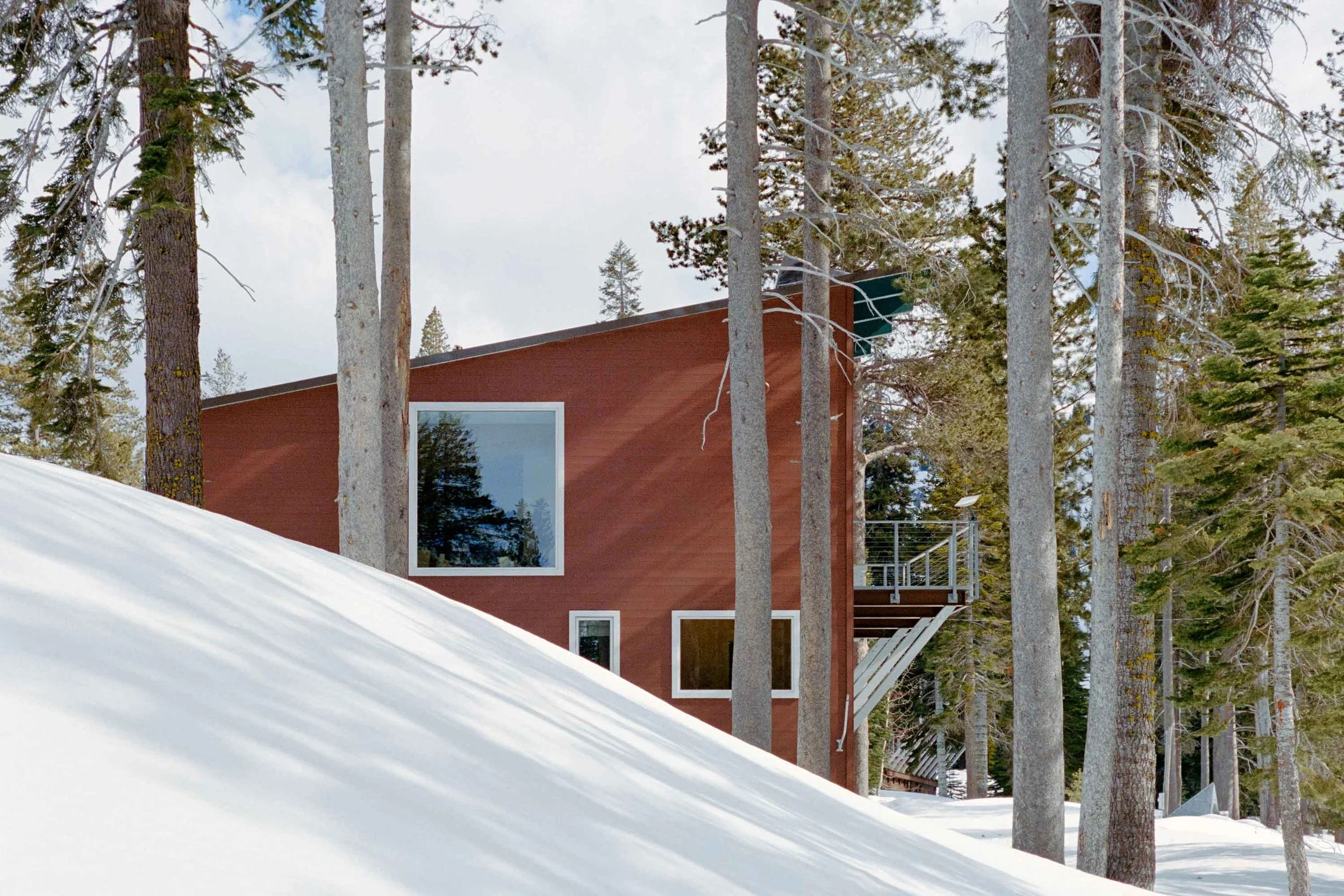 Modern mountain home exterior with natural wood, stone materials, and seamless integration into the alpine landscape