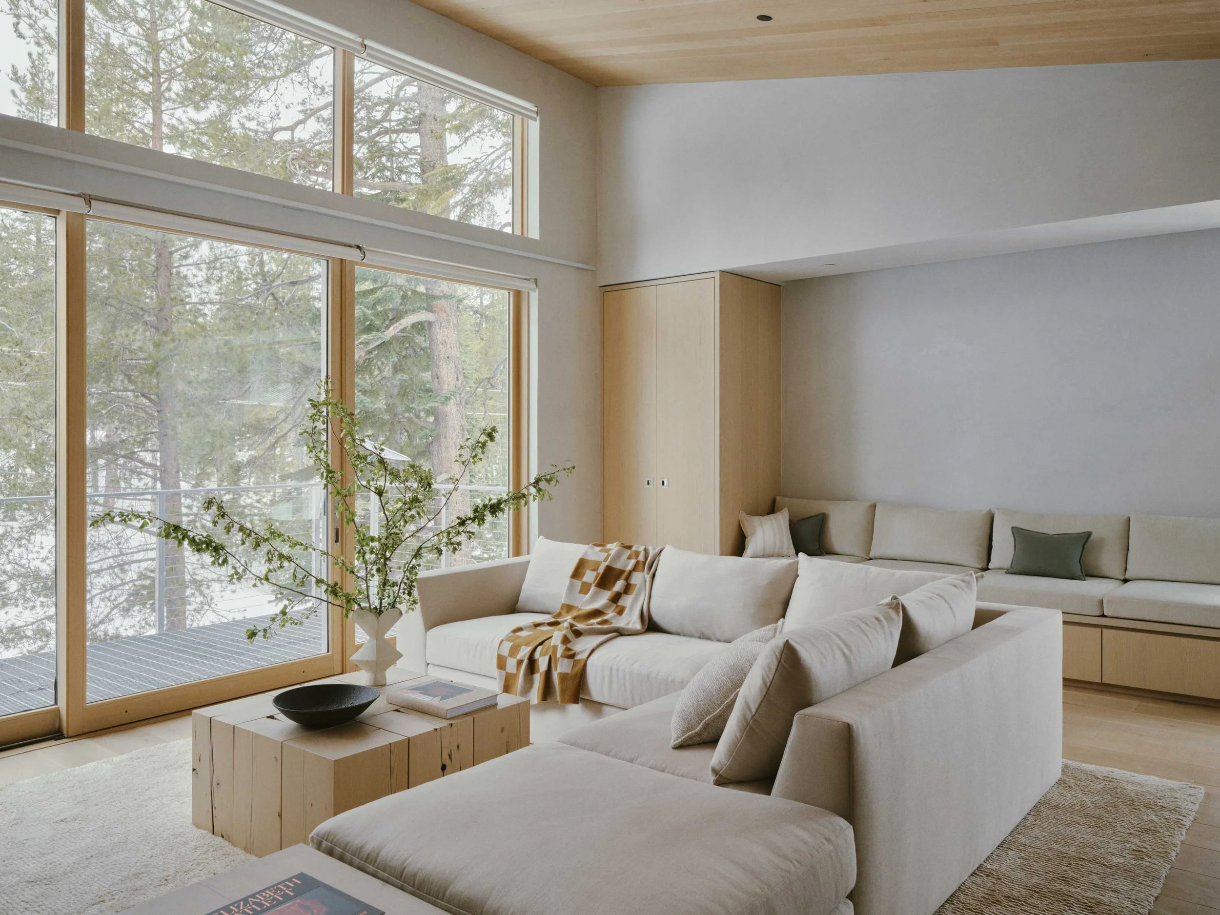 Luxury alpine living room with neutral tones, layered textures, sculptural furniture, and large windows overlooking a mountain landscape