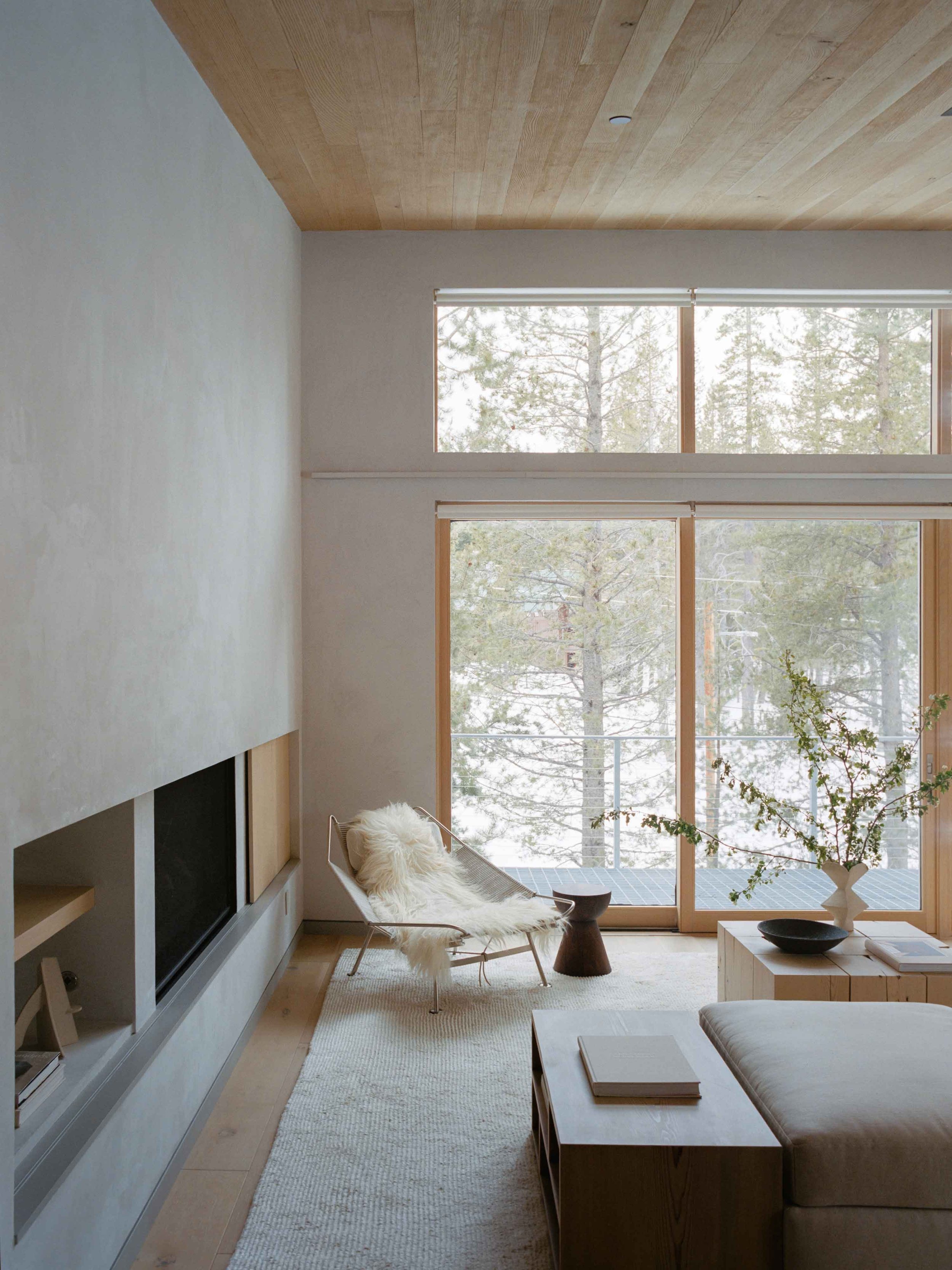 Luxury alpine living room with neutral tones, layered textures, sculptural furniture, and large windows overlooking a mountain landscape
