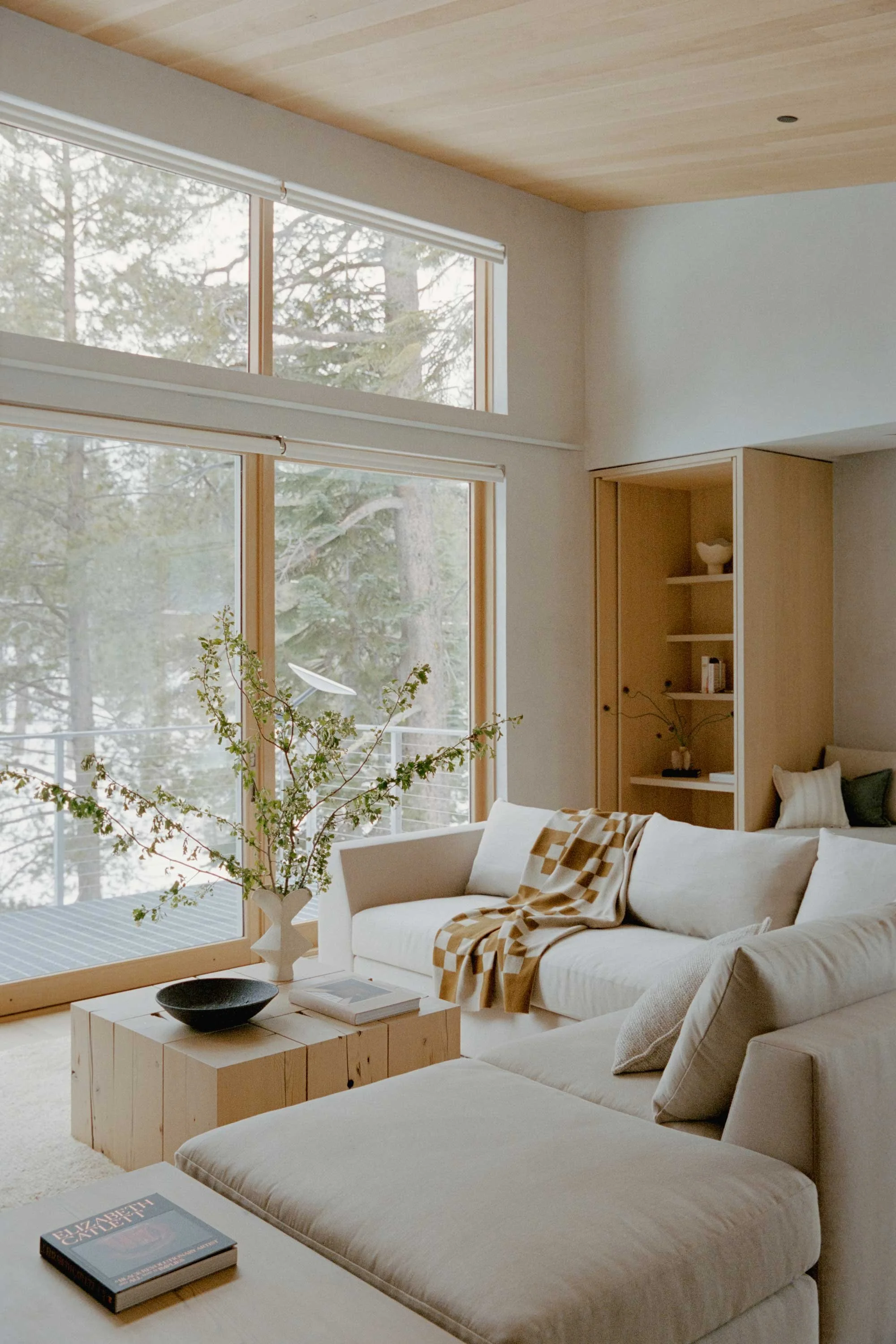 Luxury alpine living room with neutral tones, layered textures, sculptural furniture, and large windows overlooking a mountain landscape