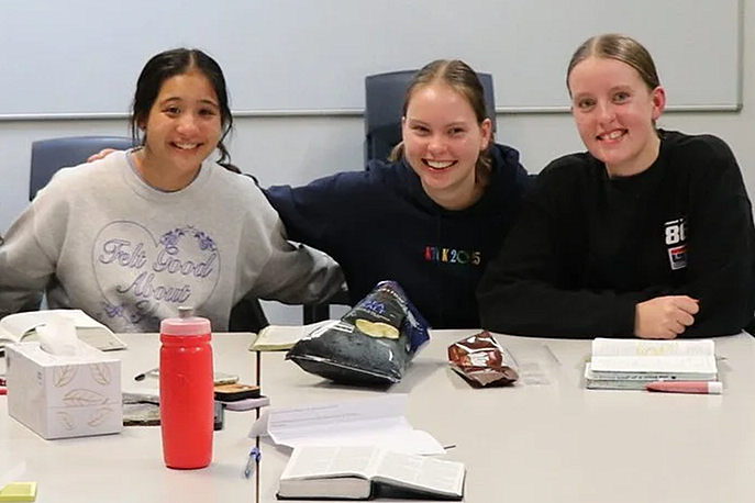3 MOBsters sitting at a table with open bibles, snacks, and a tissue box, smiling at the camera.