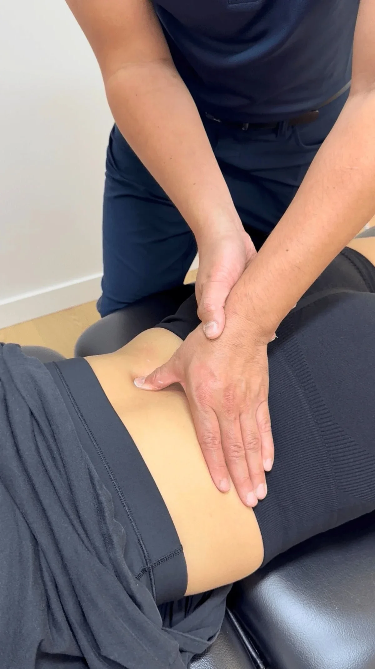 A person receiving chiropractic or physical therapy treatment on their lower back, with a therapist or healthcare professional applying pressure with hands.