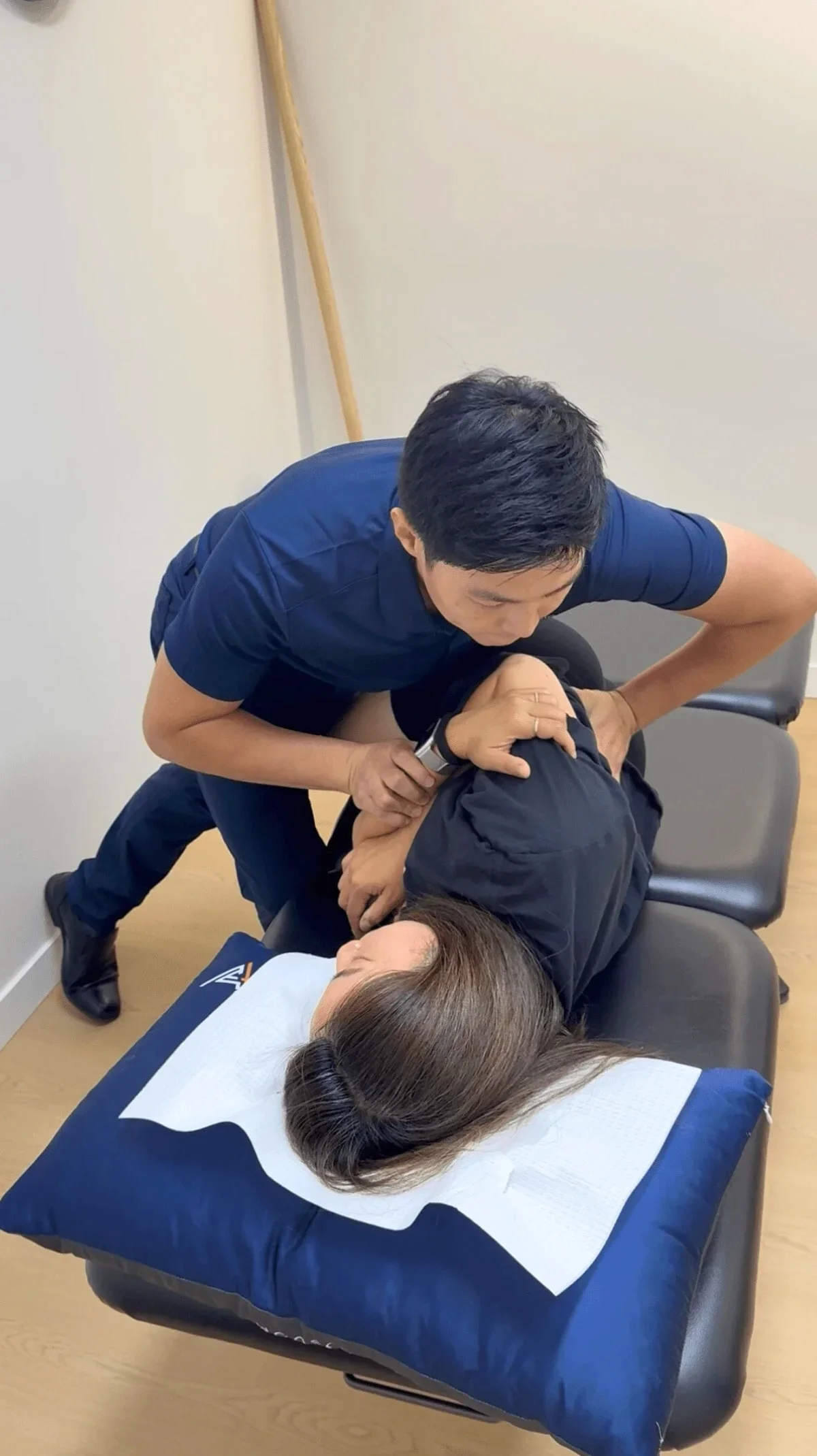 A chiropractor adjusting a woman's neck during a session while she lies face-up on a treatment table in a clinic.