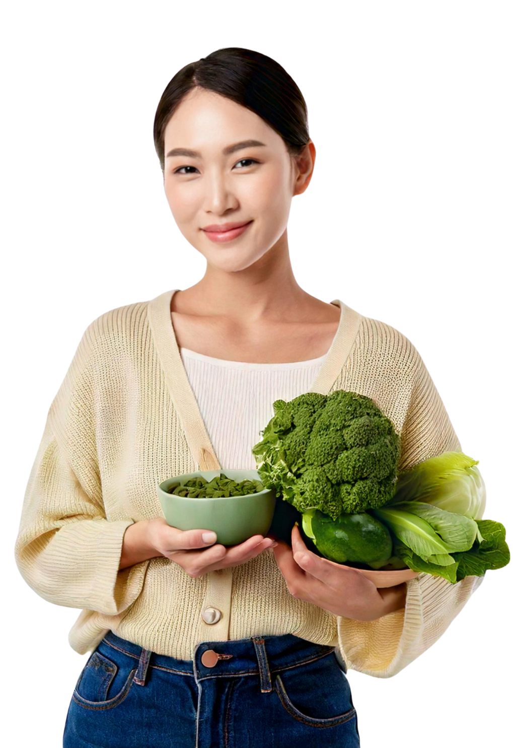 A woman holding a bowl of greens and a bowl of broccoli and leafy vegetables, smiling in a beige cardigan and jeans.