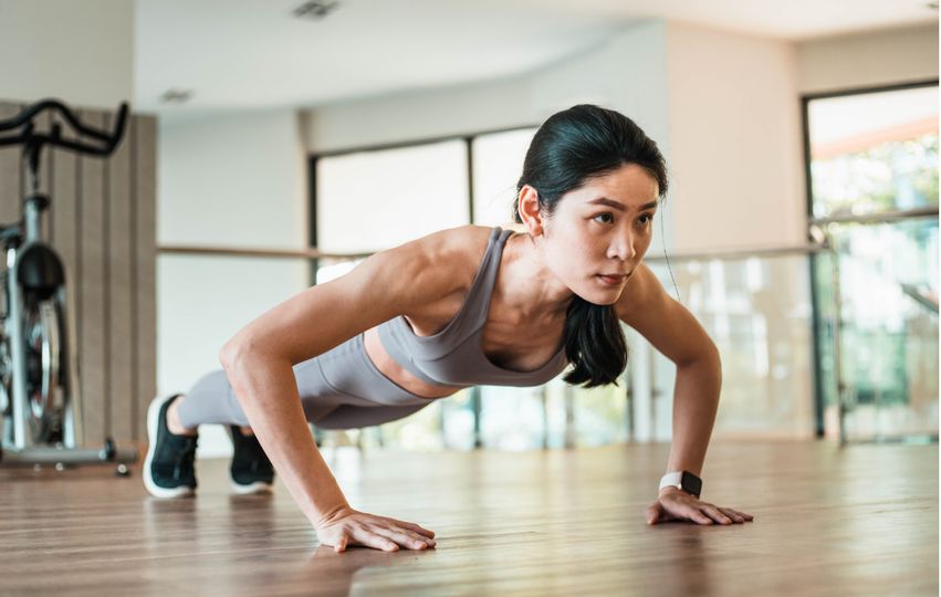 Woman doing push-up in a gym or fitness studio with wooden floors and large windows