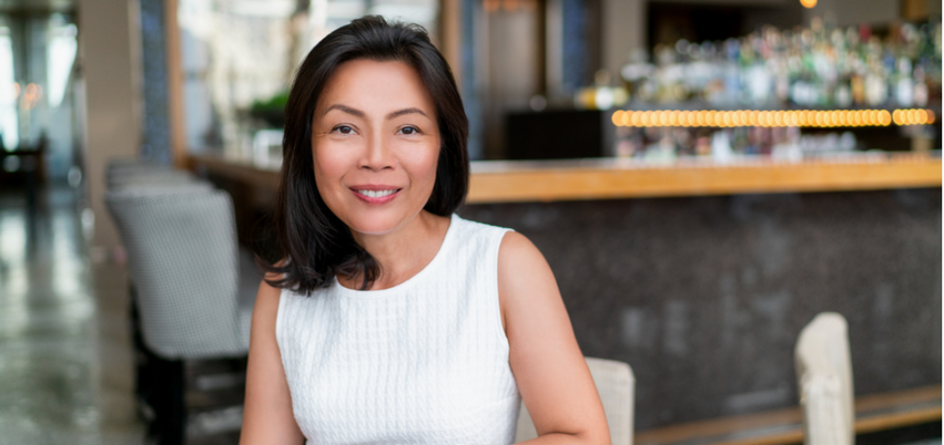 Smiling woman with shoulder-length dark hair sitting in a restaurant or cafe.