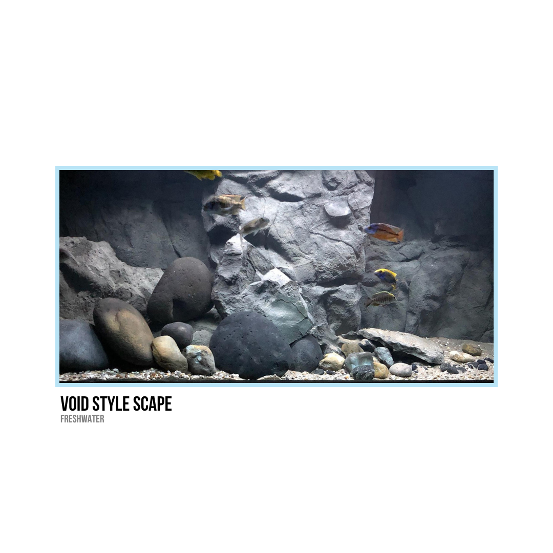 An aquarium with large rocks, smaller stones, and a rocky background, containing several small fish swimming.