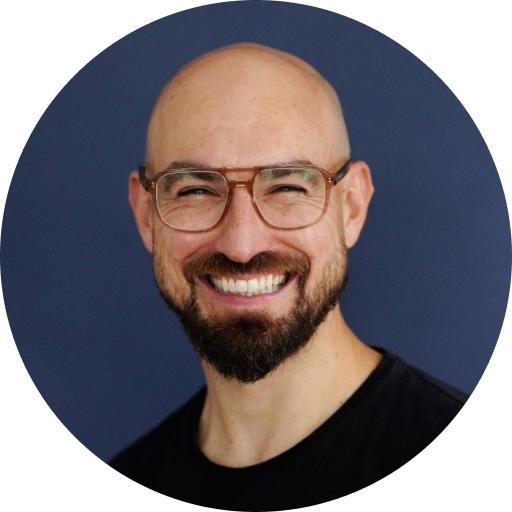 A smiling man with glasses and a beard against a dark background.