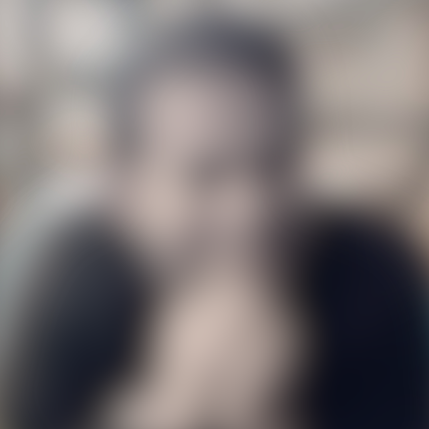 A blurry black and white photo of a woman wearing glasses, holding a phone to her ear, and smiling.