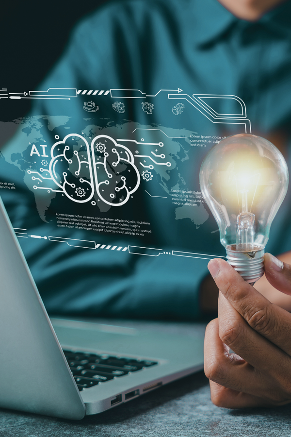 Person holds a glowing lightbulb with futuristic AI and brain graphics and technical diagrams projected above a laptop, symbolizing artificial intelligence and innovation.
