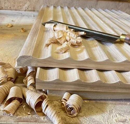 Woodworking scene with carved wooden panels, a chisel, and wood shavings on a workbench.