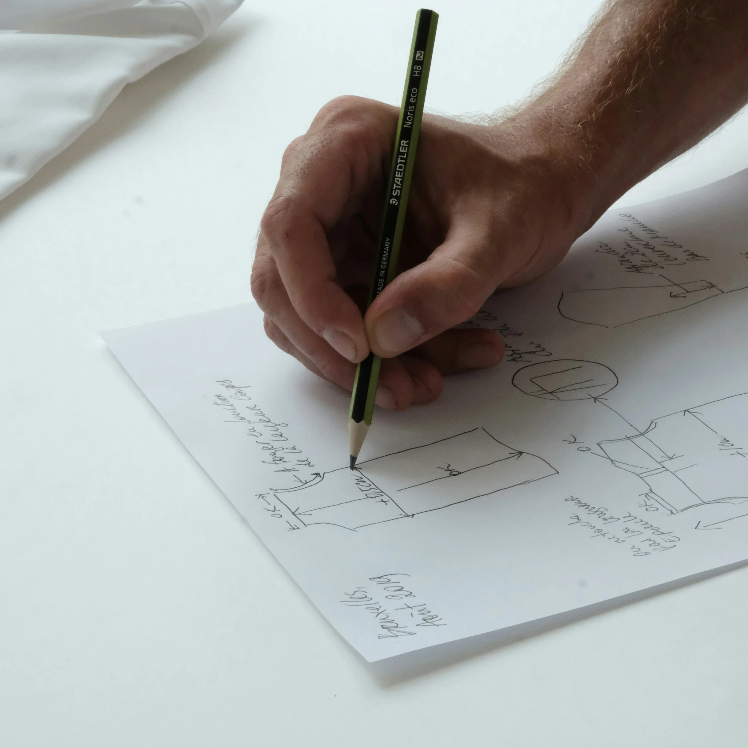 A person's hand holding a yellow and black colored pencil writing on a piece of white paper with handwritten text and a tree sketch.