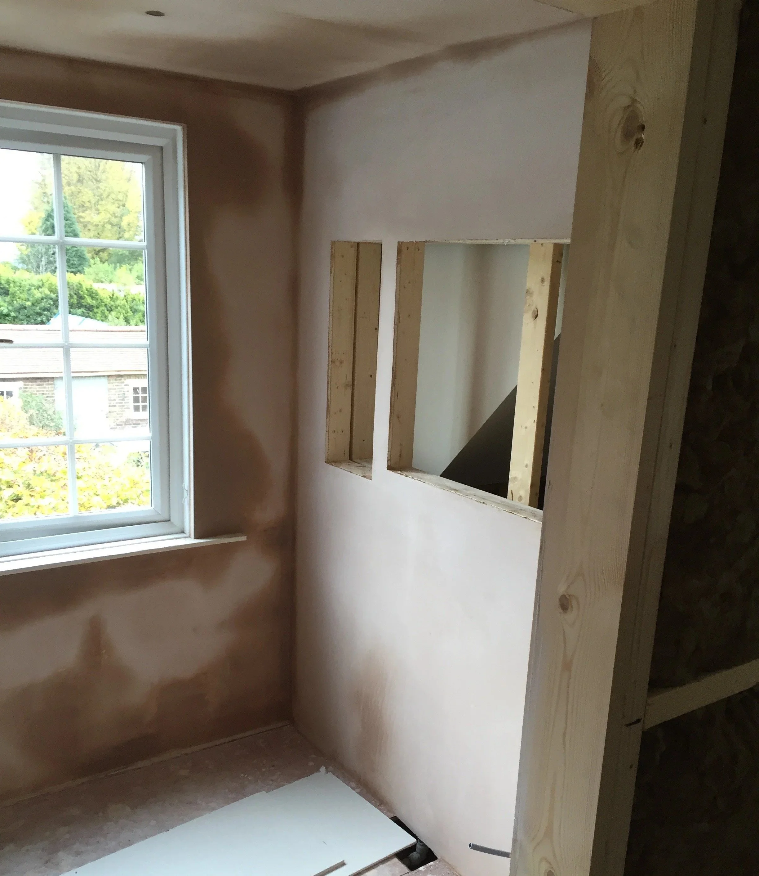 Construction or renovation area with partial wall framing and a window showing a tree outside.