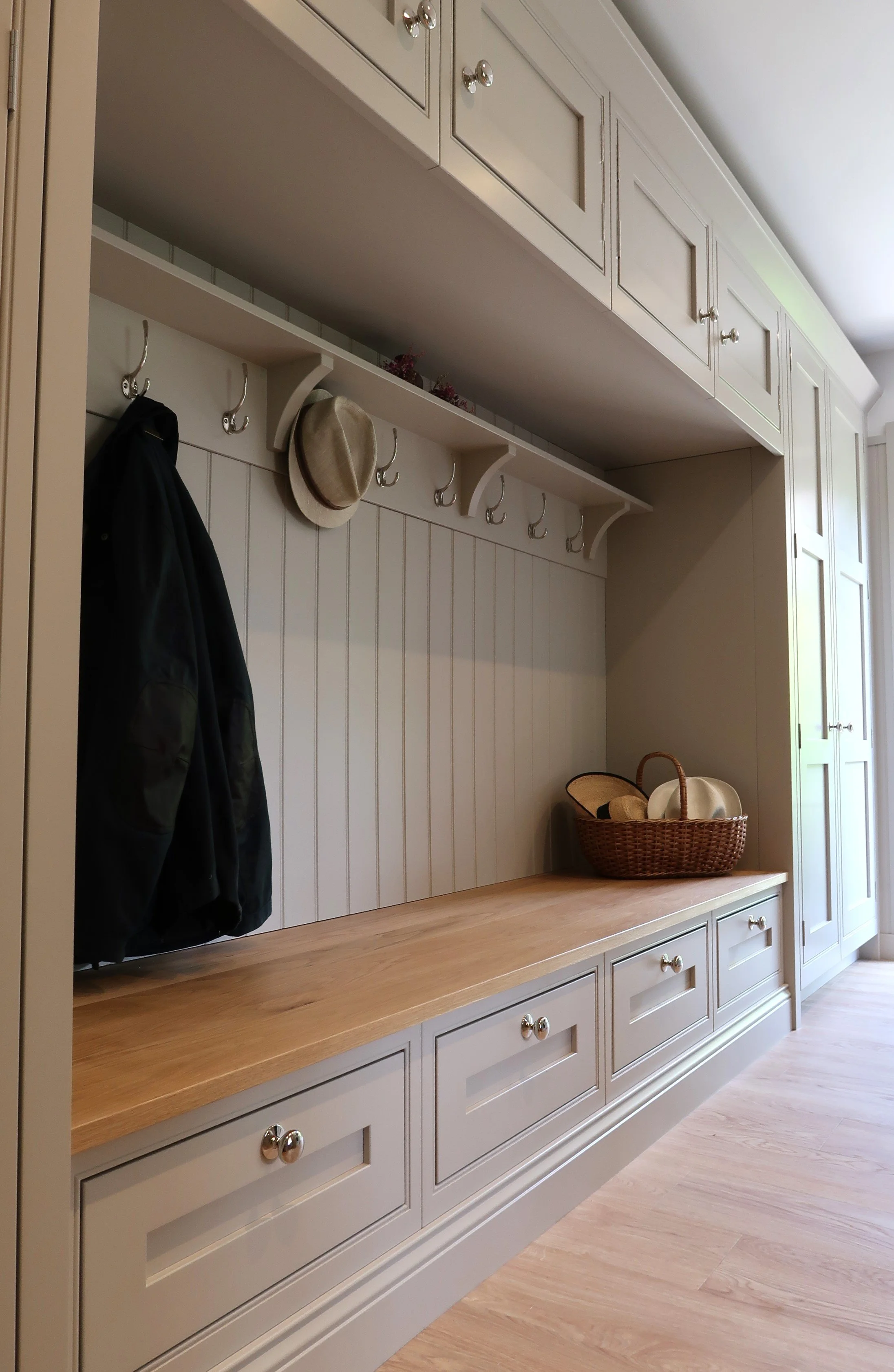 A white built-in entryway organization with cabinets, a wooden countertop, a row of hooks with hanging items, a basket, and a door on the right side.