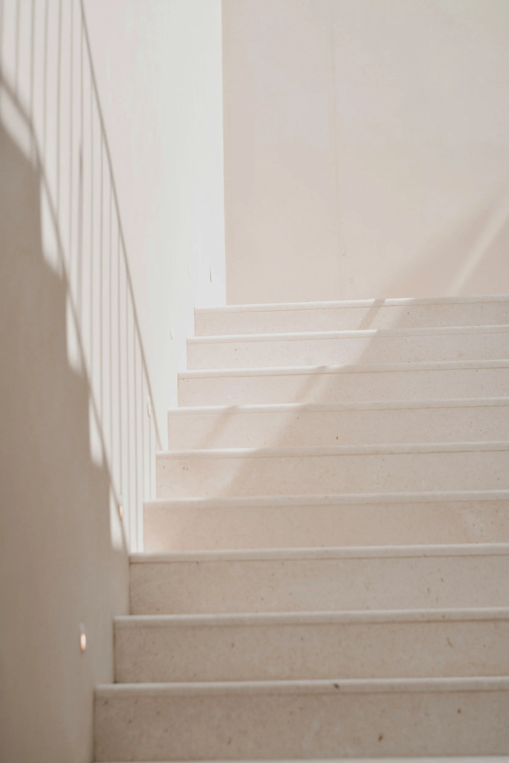 Staircase with beige steps and white walls, viewed from the bottom looking up with light shining down.