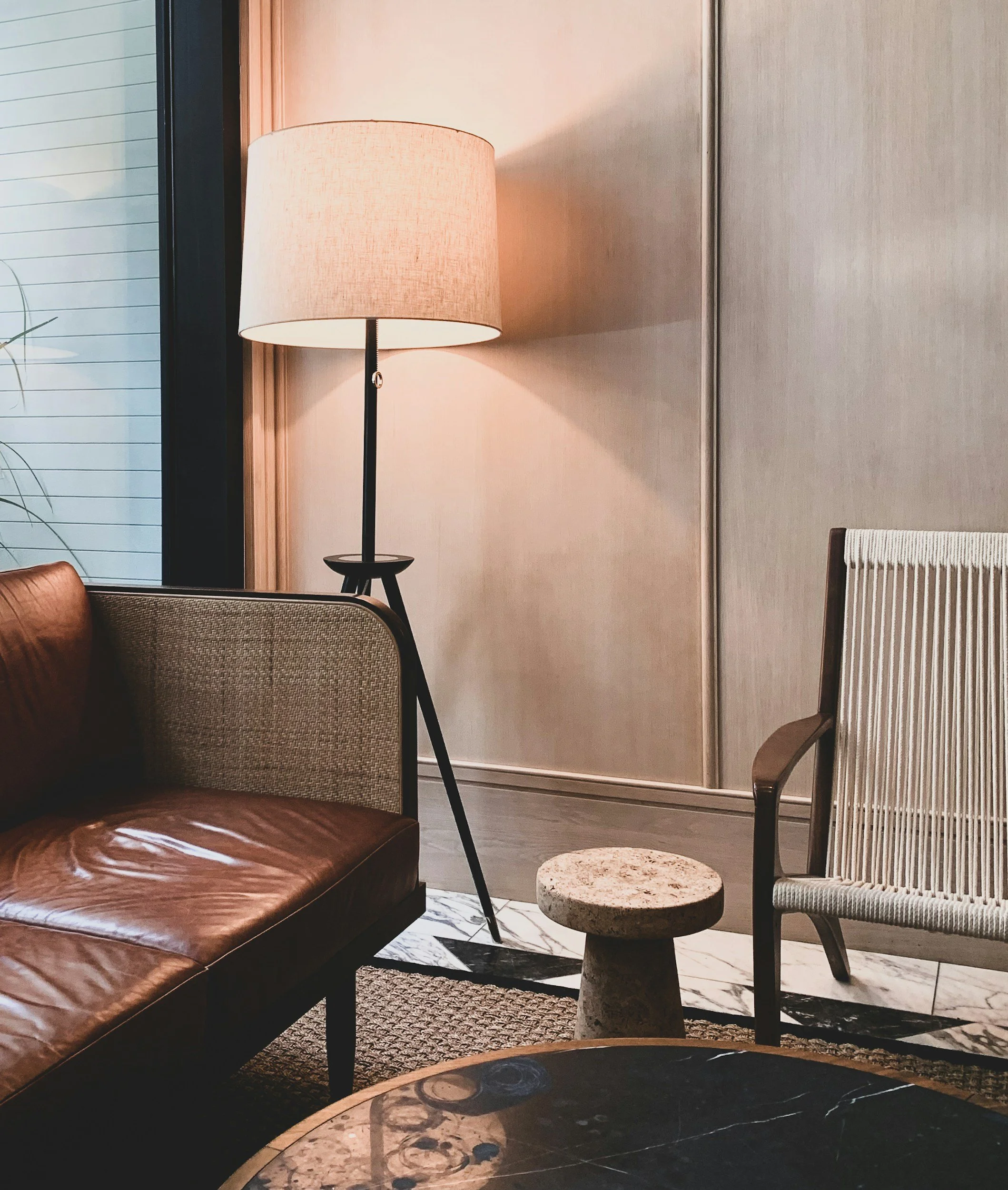 Psychotherapy office with a brown leather sofa, beige upholstered armchair, small marble-topped side table, a marble coffee table, a floor lamp with a beige shade, and a wave-patterned rug.