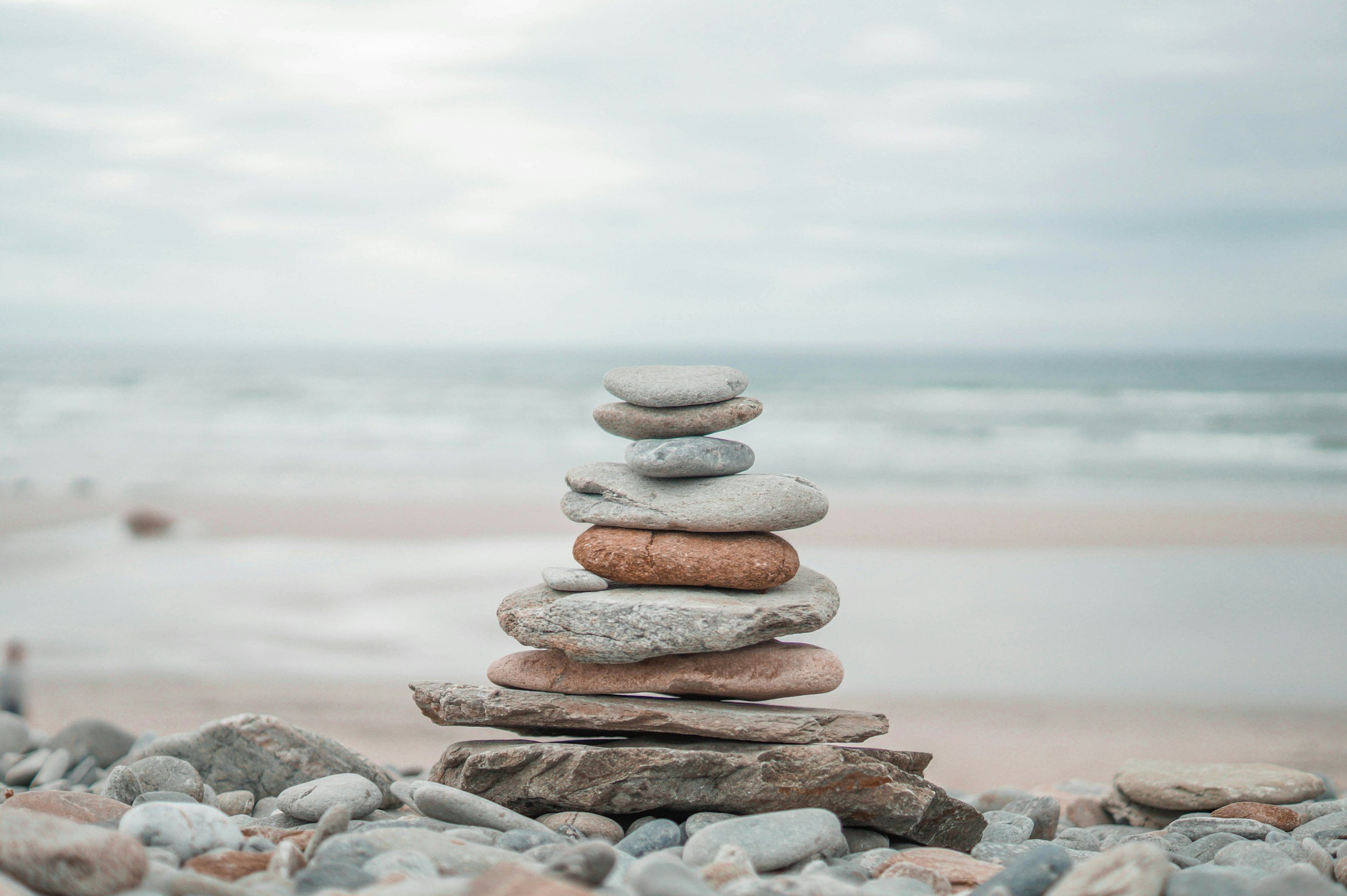 Stacked rocks on a beach with the ocean and cloudy sky in the background.