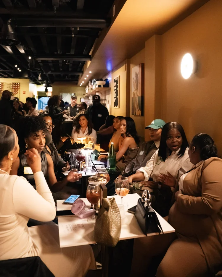 Group of people sitting at a table in a lively restaurant, engaging in conversation and enjoying drinks.