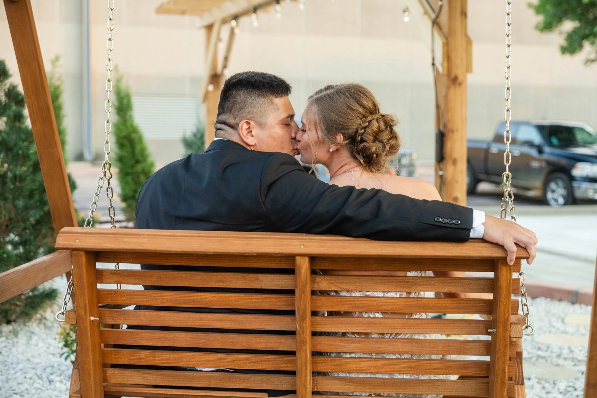 Bride and groom sitting together on a wooden swing outside LuxeFalls Venue in Sioux Falls, South Dakota. A romantic outdoor photo capturing love and natural beauty at this modern wedding venue.