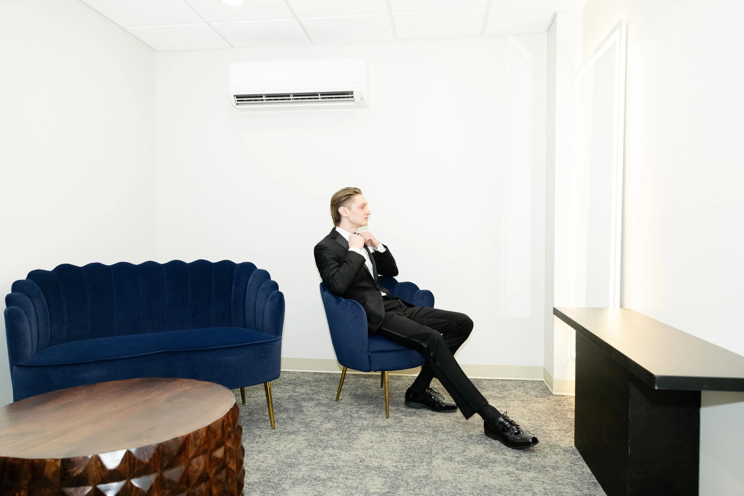 Groom relaxing in the modern groom suite at LuxeFalls Venue in Sioux Falls, South Dakota, featuring a navy-blue couch and minimalist design — a comfortable space for getting ready before the wedding.