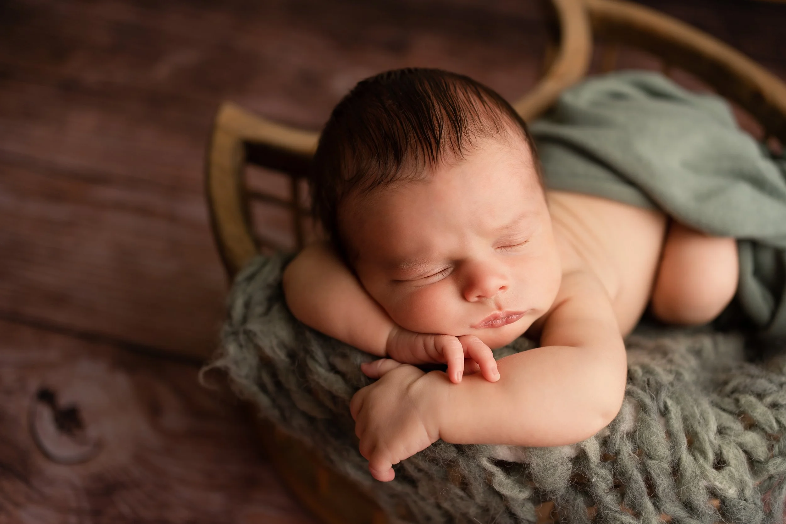 A sleeping baby with dark hair lying on a soft blanket, resting his head on his arm.
