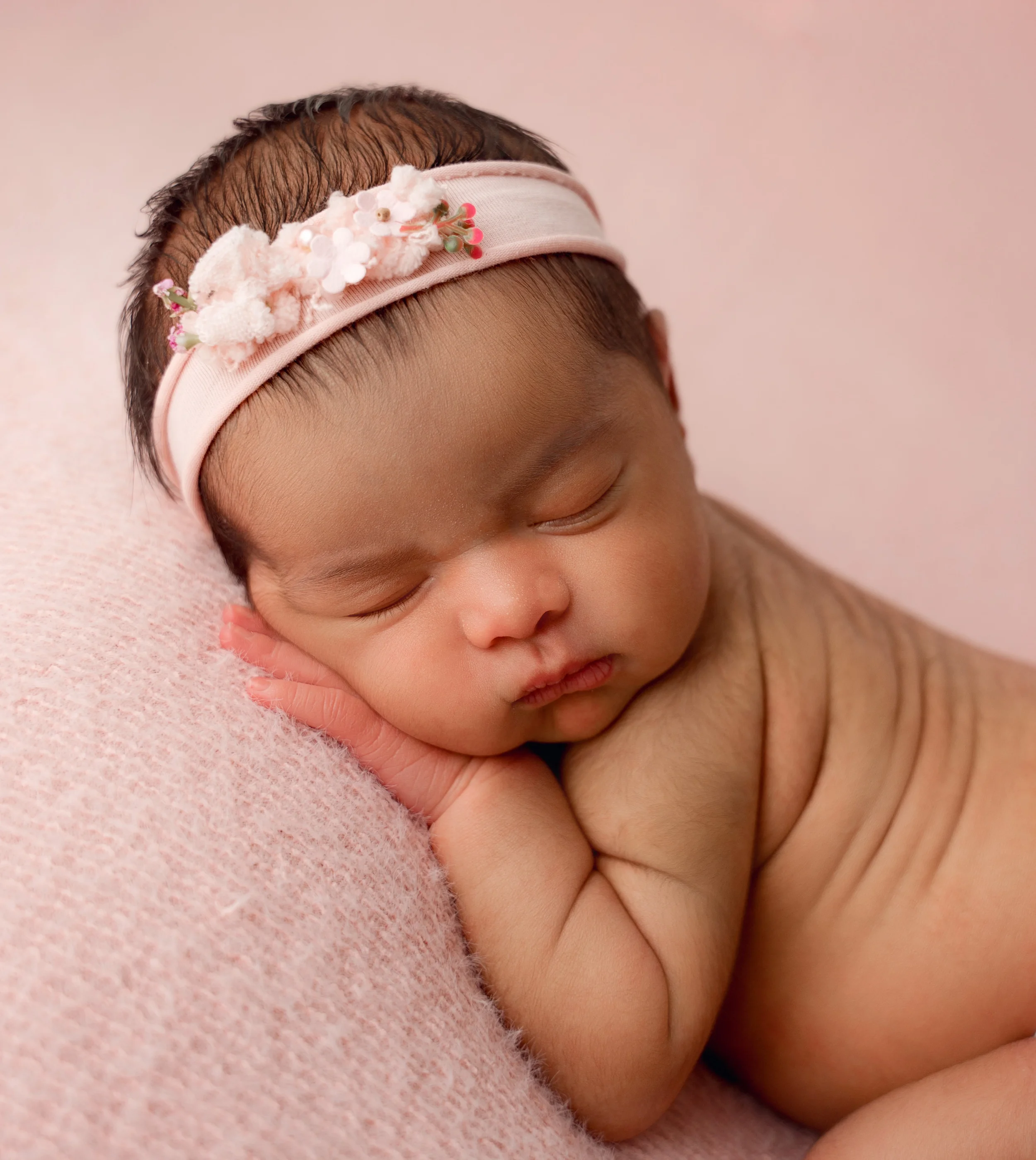 baby girl with floral headband posed on pink fabric in studio during session with raleigh newborn photographer