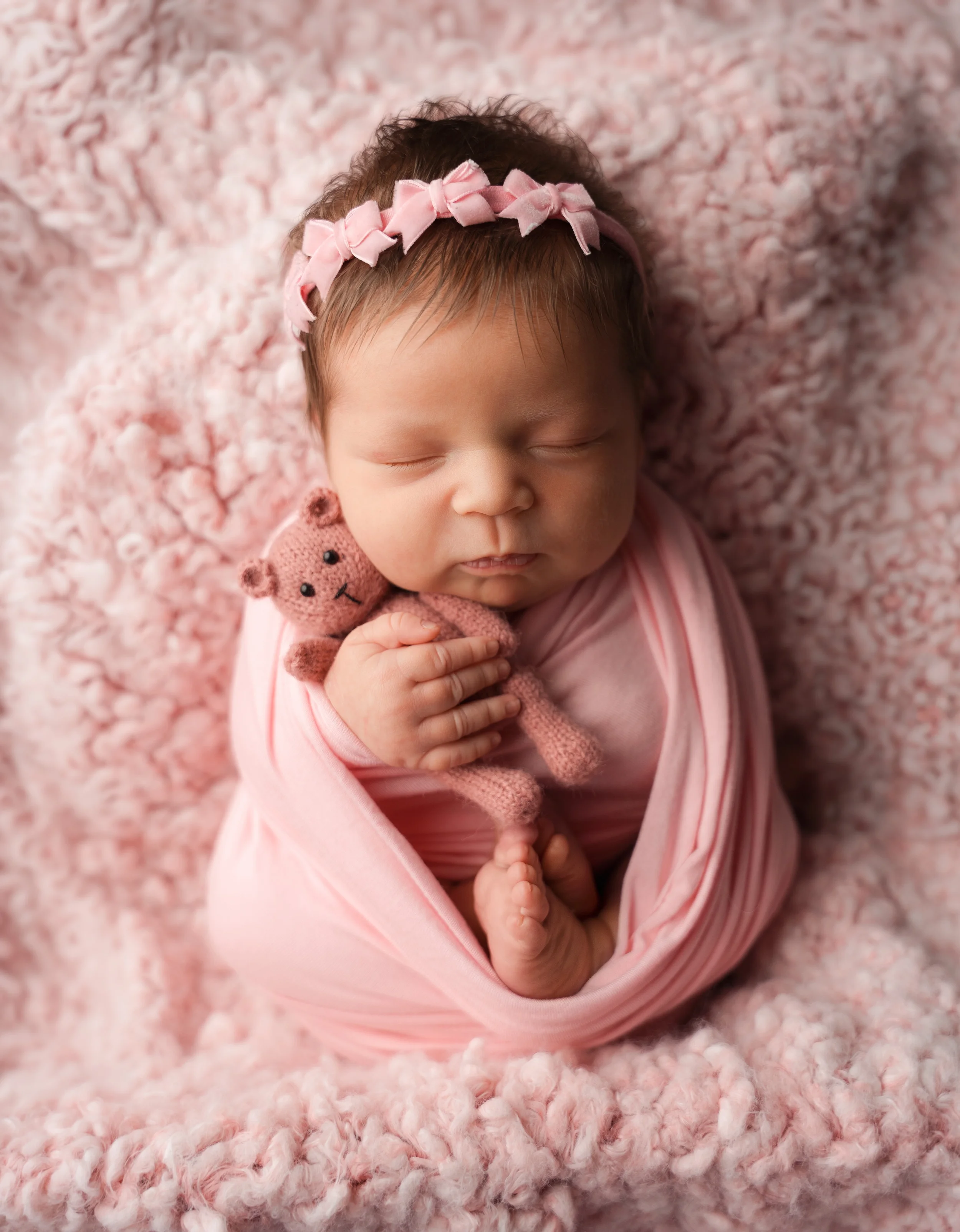 newborn girl holding bear stuffy wrapped in pink with a pink ribbon head band during session with raleigh newborn photographer