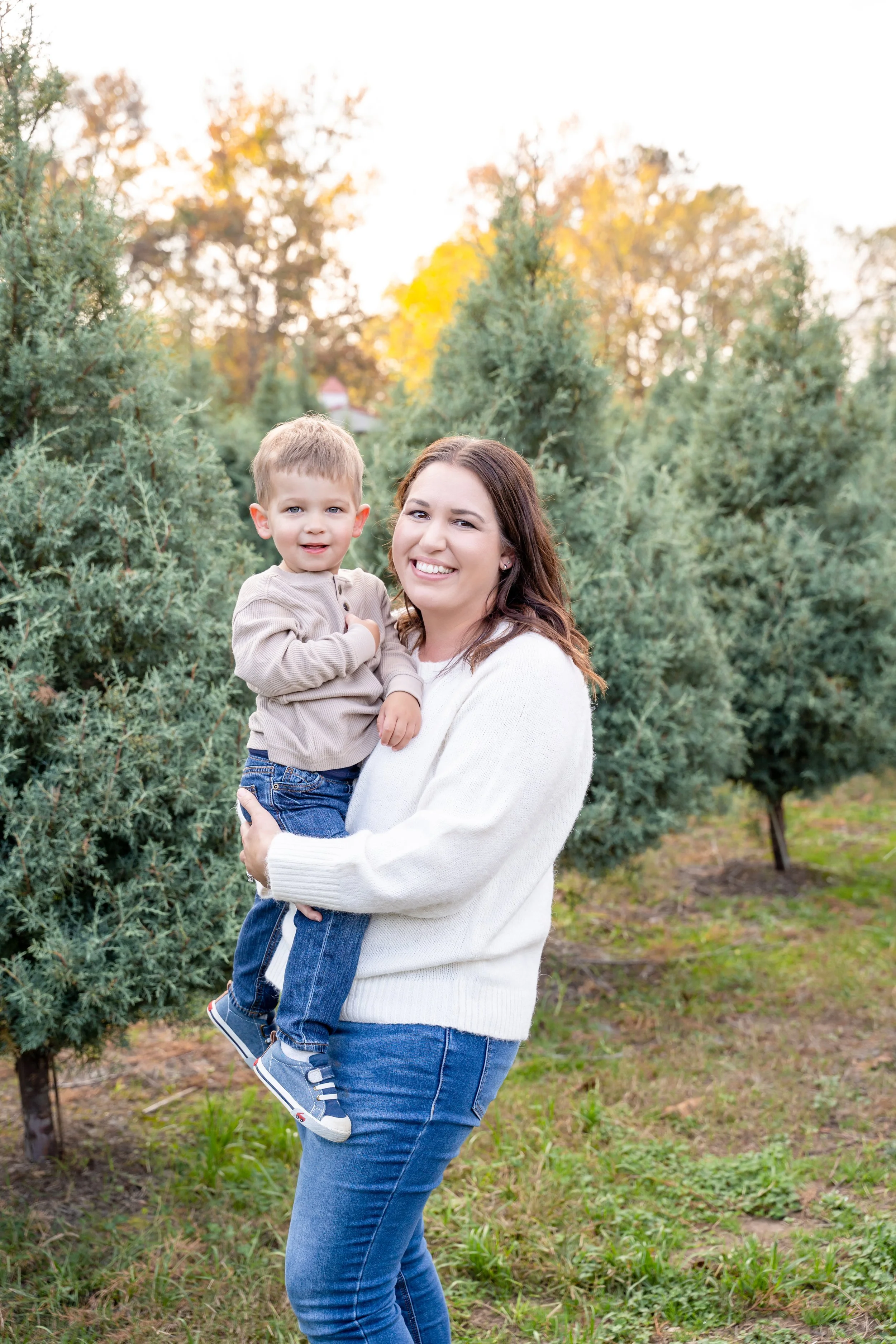 A woman smiling and holding a young boy in a christmas tree farm setting during session with raleigh family photographer