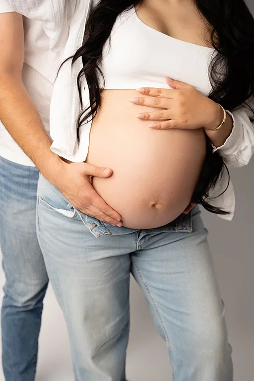 mom and dad posed with mom's baby bump showing wearing jeans during raleigh maternity photographer session