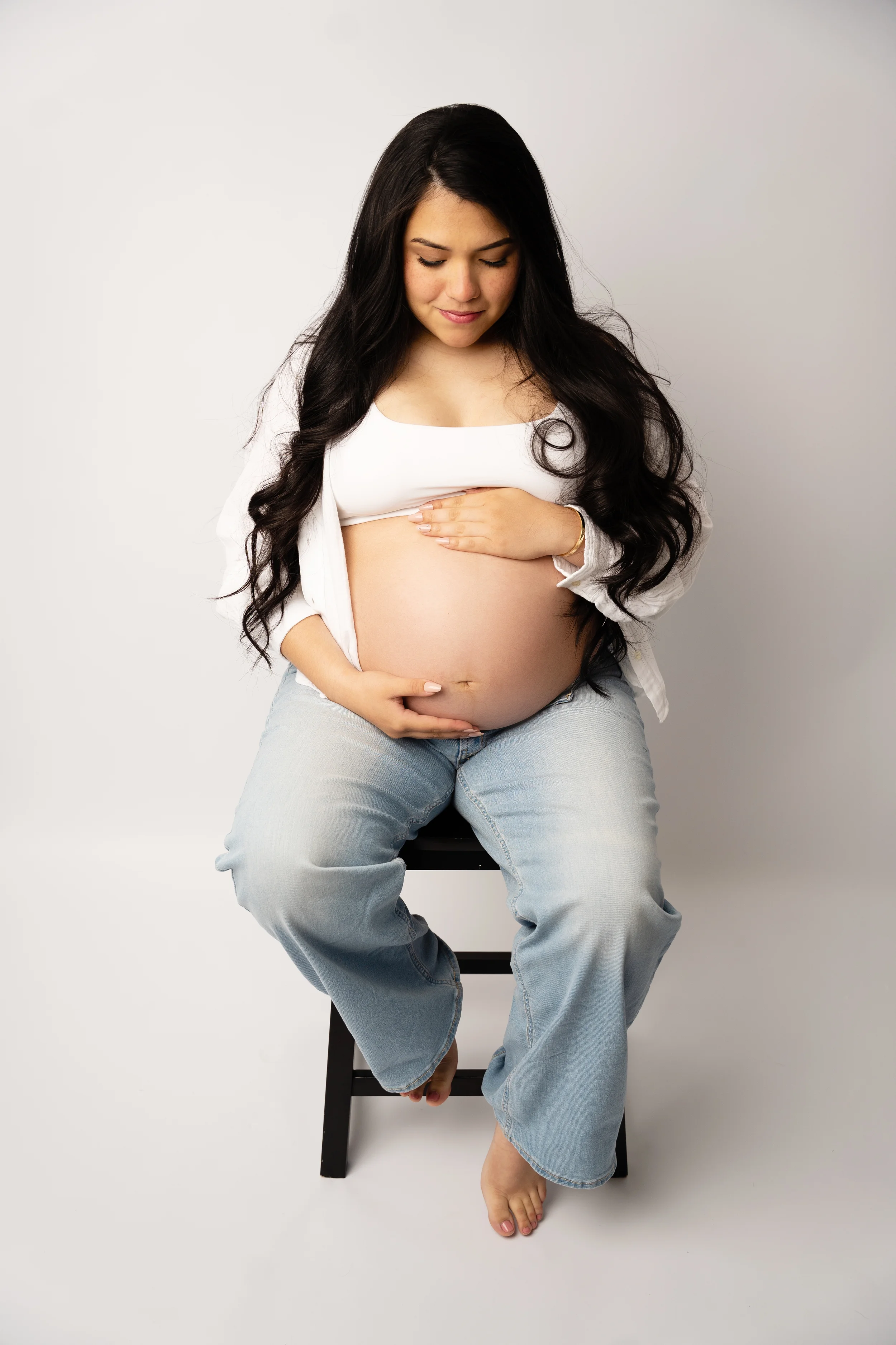 pregnant mom with white tshirt and jeans embracing her belly during session with raleigh newborn photographer