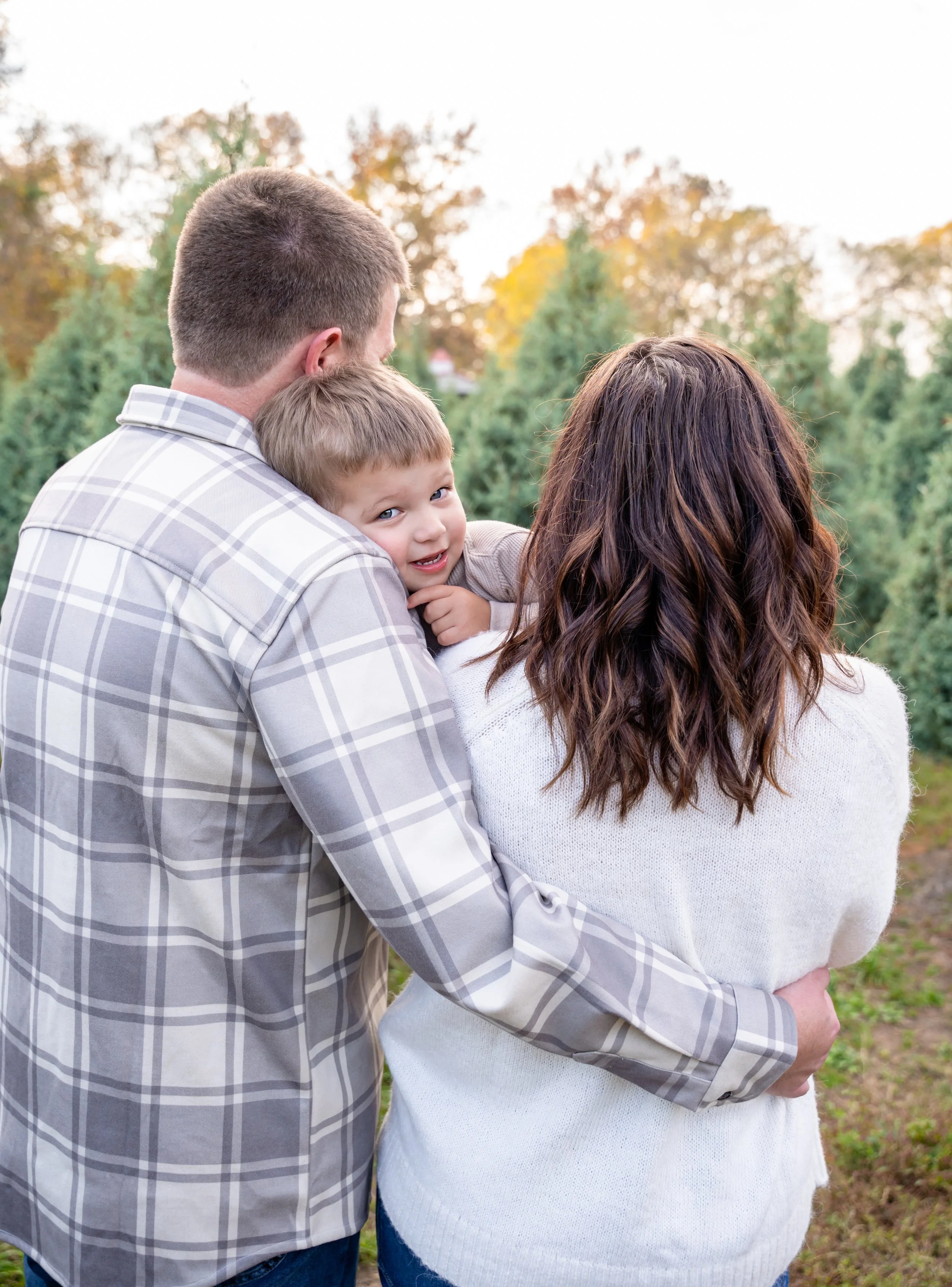 family of 3 posed at a christmas tree farm during session with raleigh family photographer