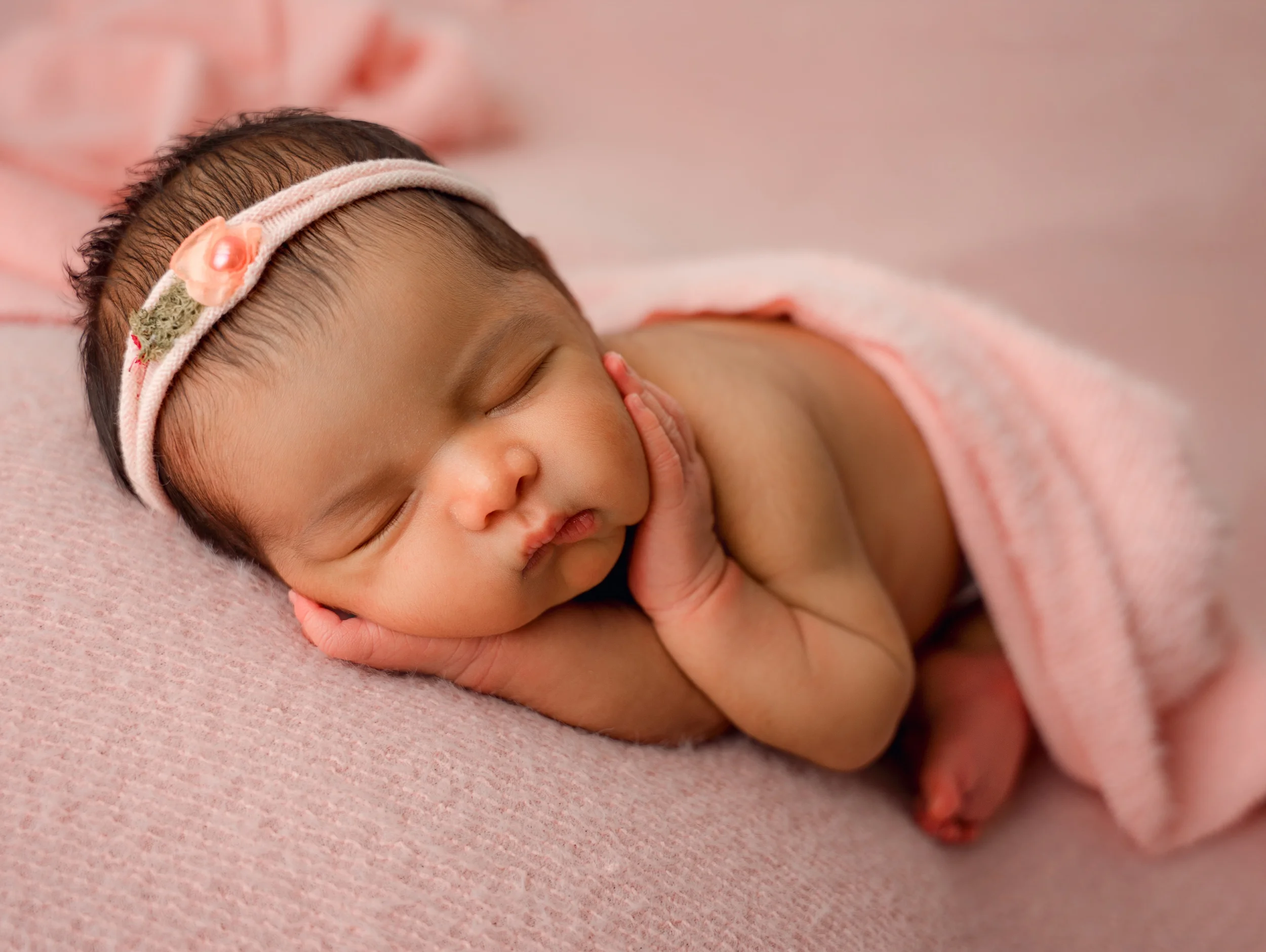 Close-up of a sleeping baby girl with a headband, lying on a pink blanket during session with Clayton newborn photographer