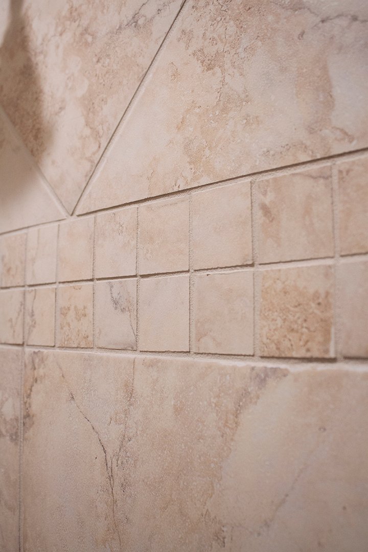 A close-up of the master bathroom shower tile showing the smaller tiles banding around the center and the larger diamond and square pattern on the rest of the wall.