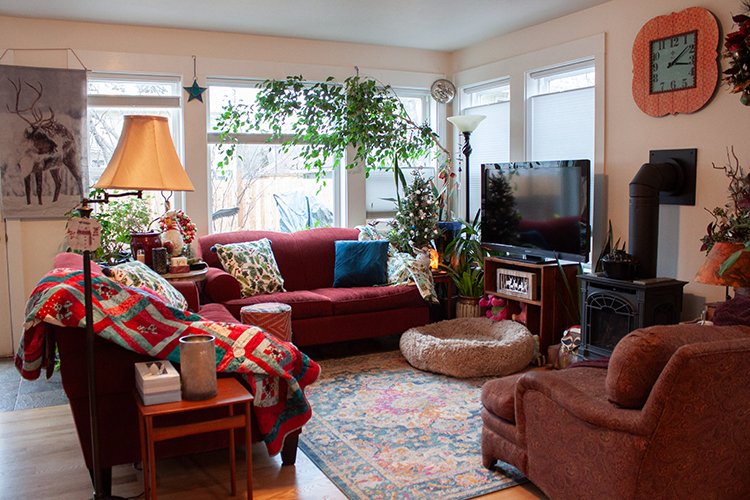 The cozy living room includes a wood stove vented to the outside of the home, large windows filling the space with natural light, and real wood floors.