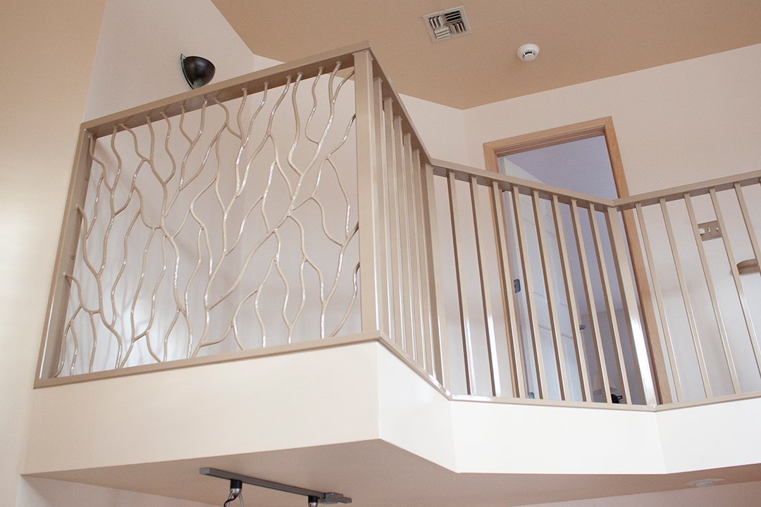 The metal stair railing overlooking the home's foyer features an intricate pattern that looks like tree branches.