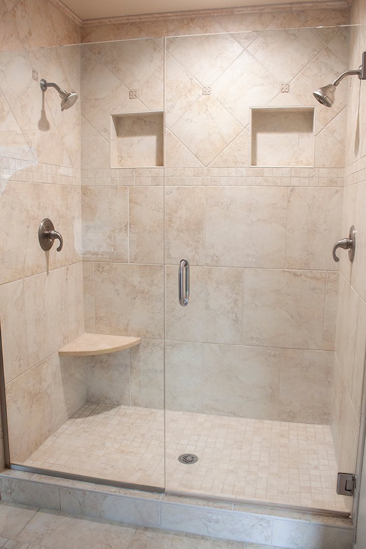 The master shower includes intricate tile patterns, showerheads on two sides and built-in shelving.